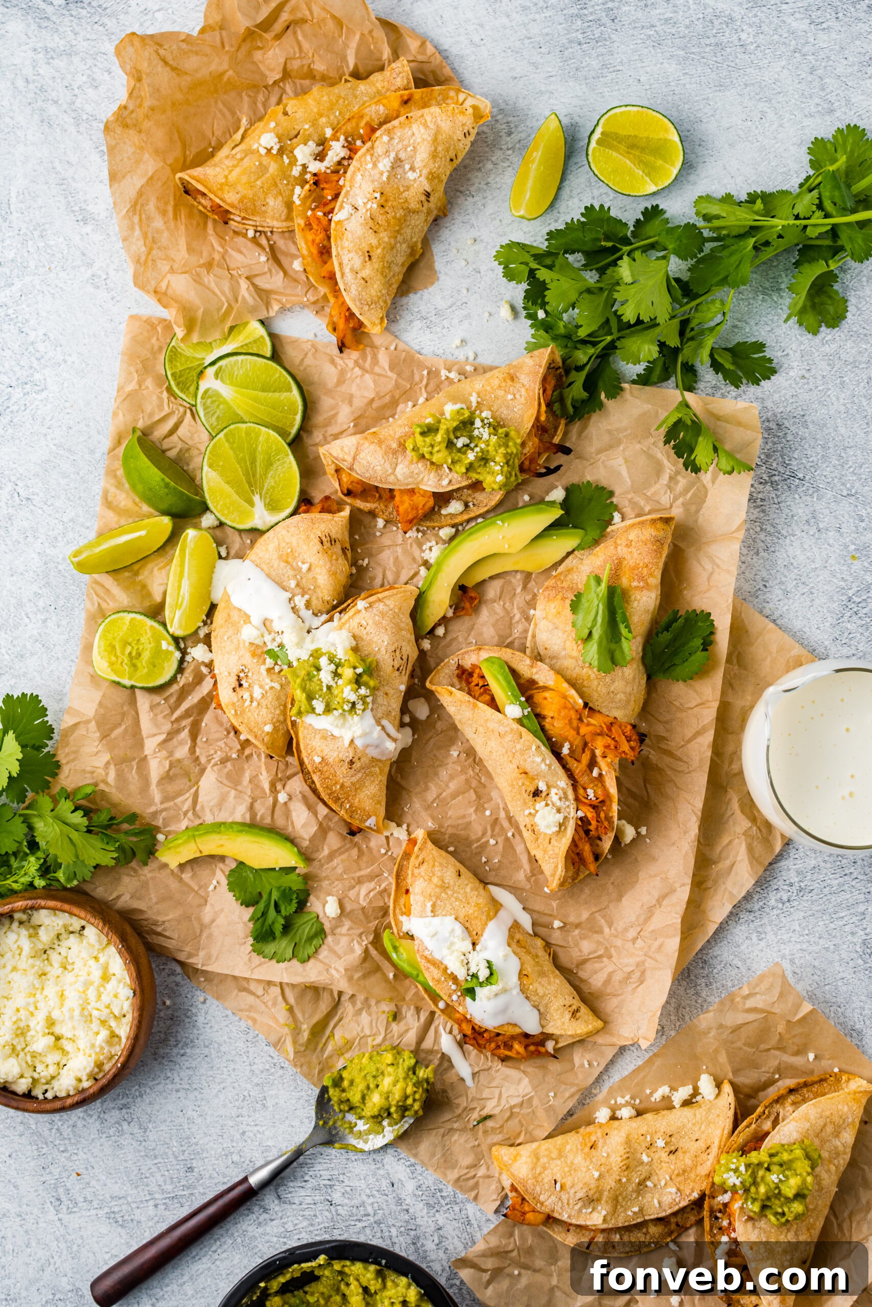 Overhead view of Crispy Tinga Tacos on a piece of parchment paper surrounded by lime and avocado slices.