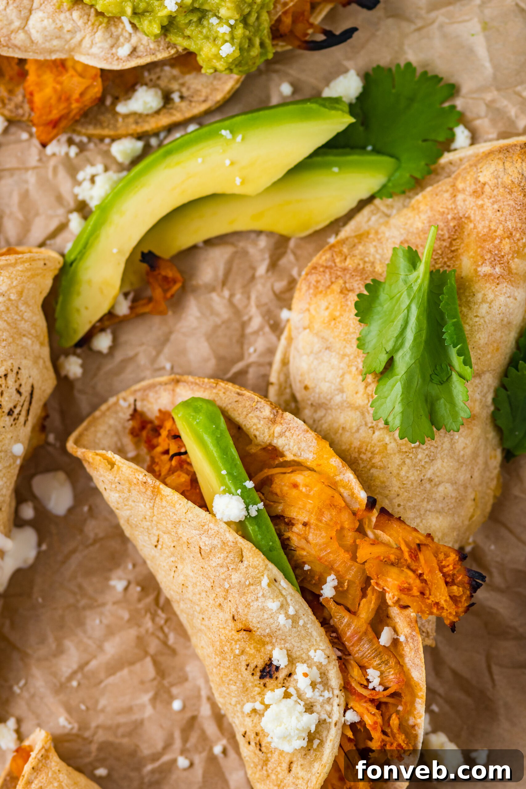 Close up view of Crispy Tinga Tacos on a piece of parchment paper surrounded by avocado slices.