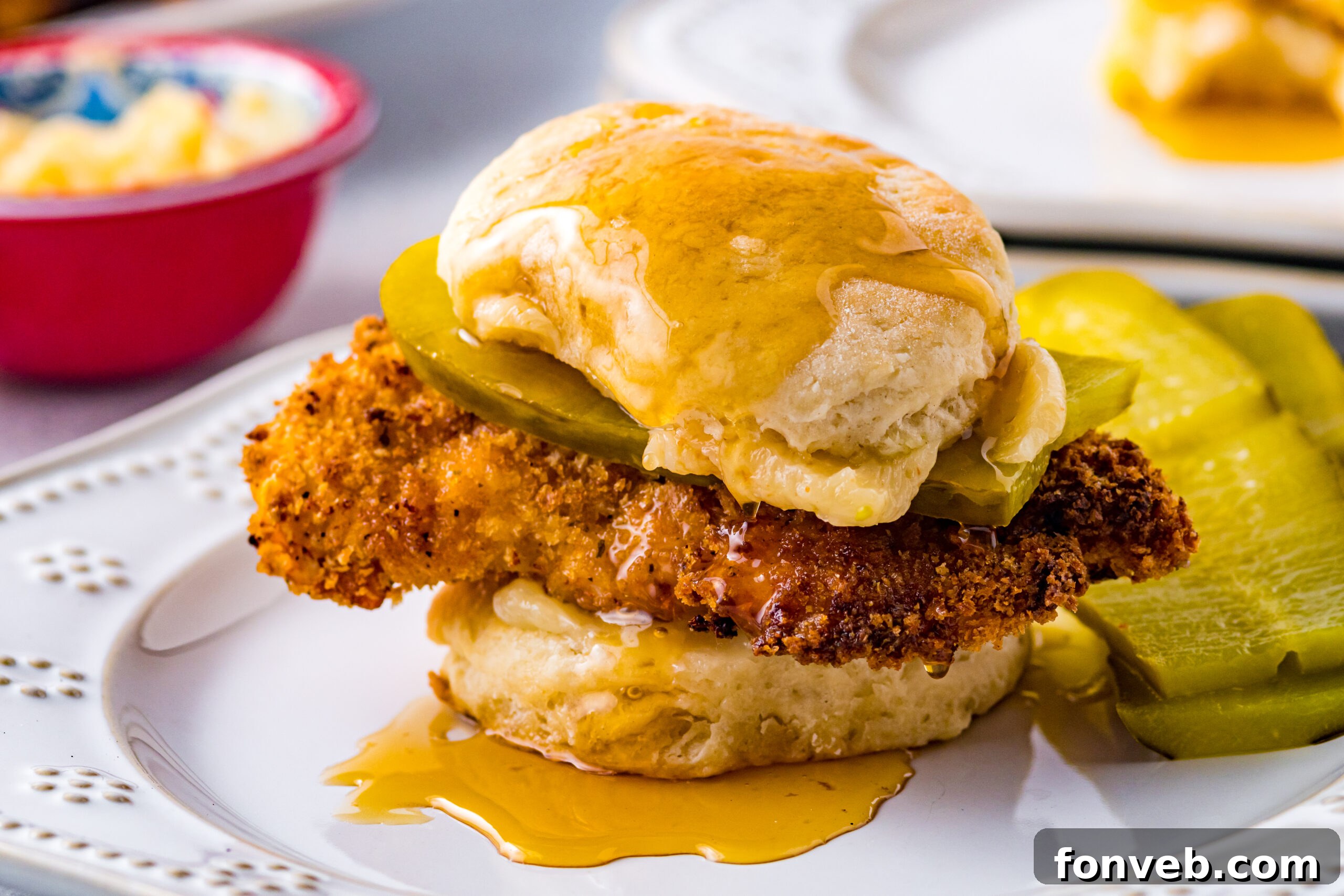 Front view of Honey Butter Chicken Biscuit on a white plate served with two pickle slices, ready to be enjoyed.