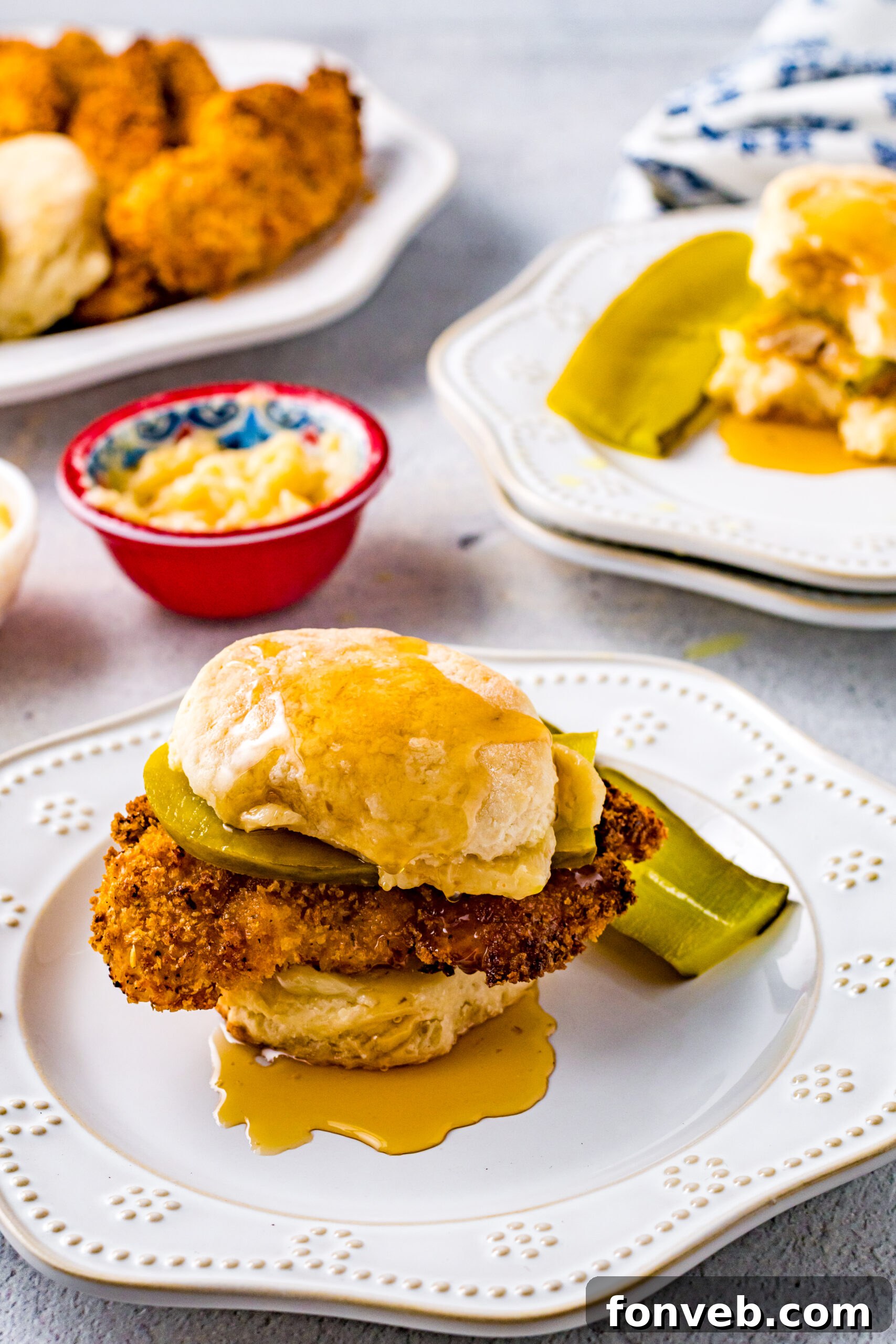 Front view of Honey Butter Chicken Biscuit on a white plate served with two pickle slices, highlighting the sweet and spicy glaze.