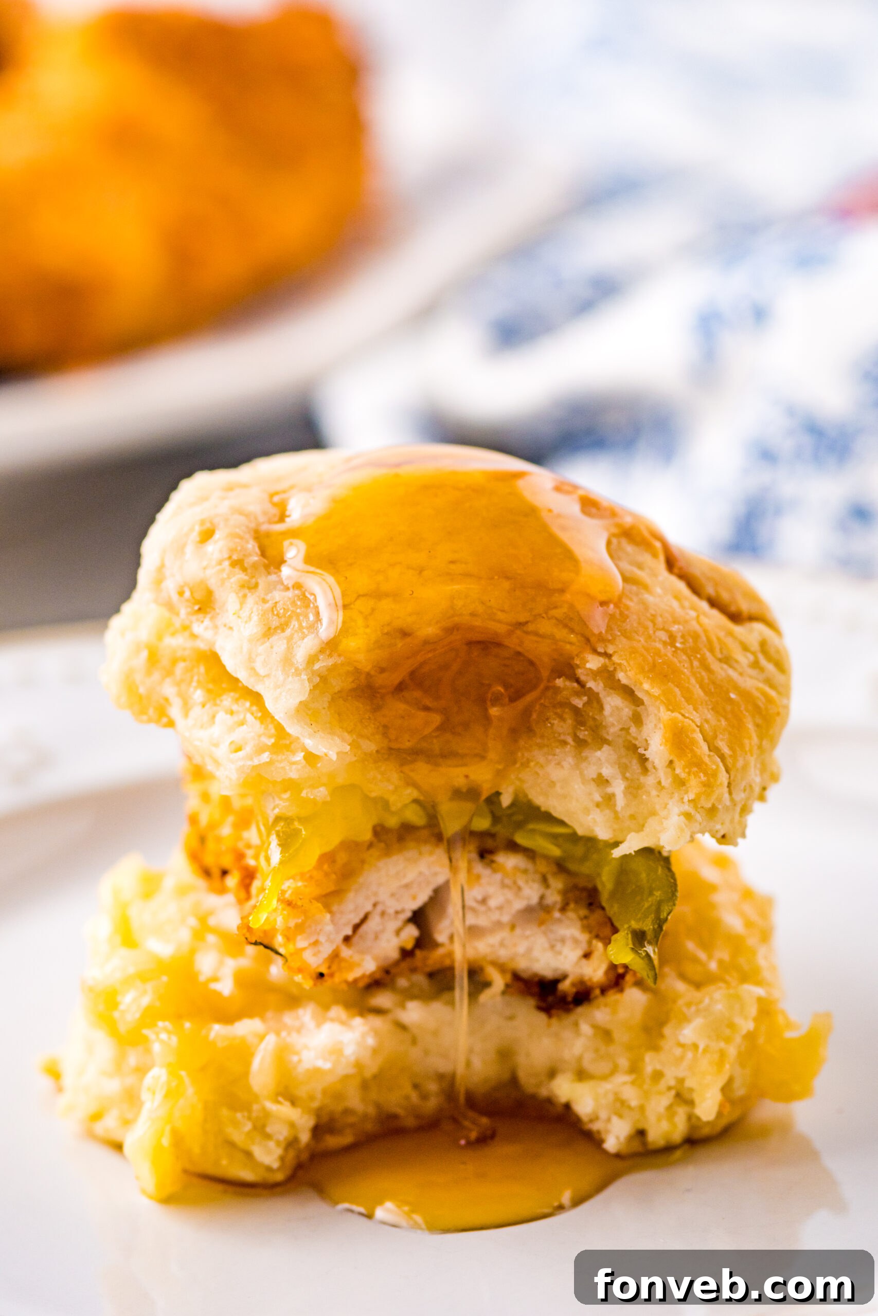Front view of Honey Butter Chicken Biscuit on a white plate with a bite removed, revealing the layers of flavor.