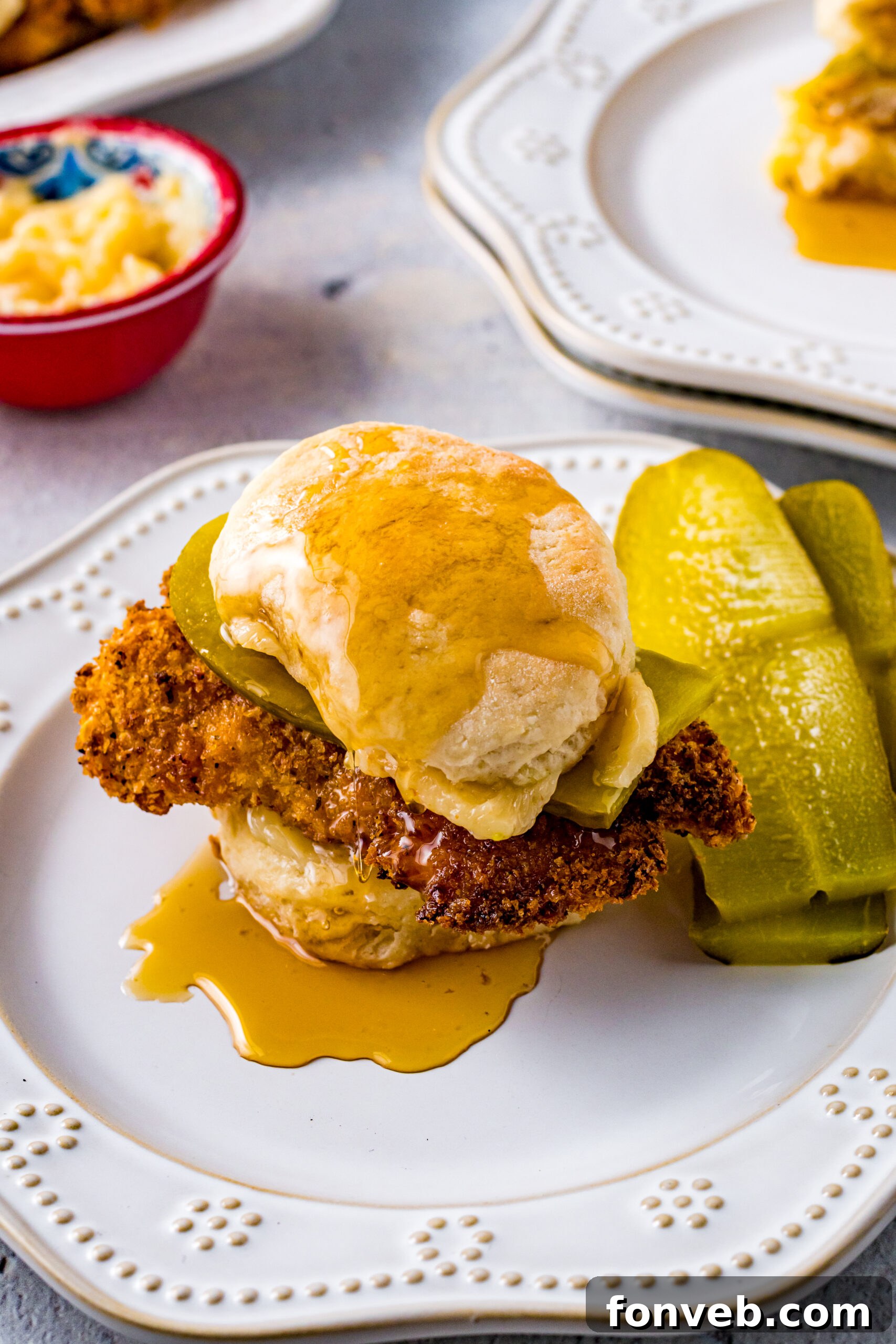 Front view of Honey Butter Chicken Biscuit on a white plate served with two pickle slices, highlighting the delicious glaze.