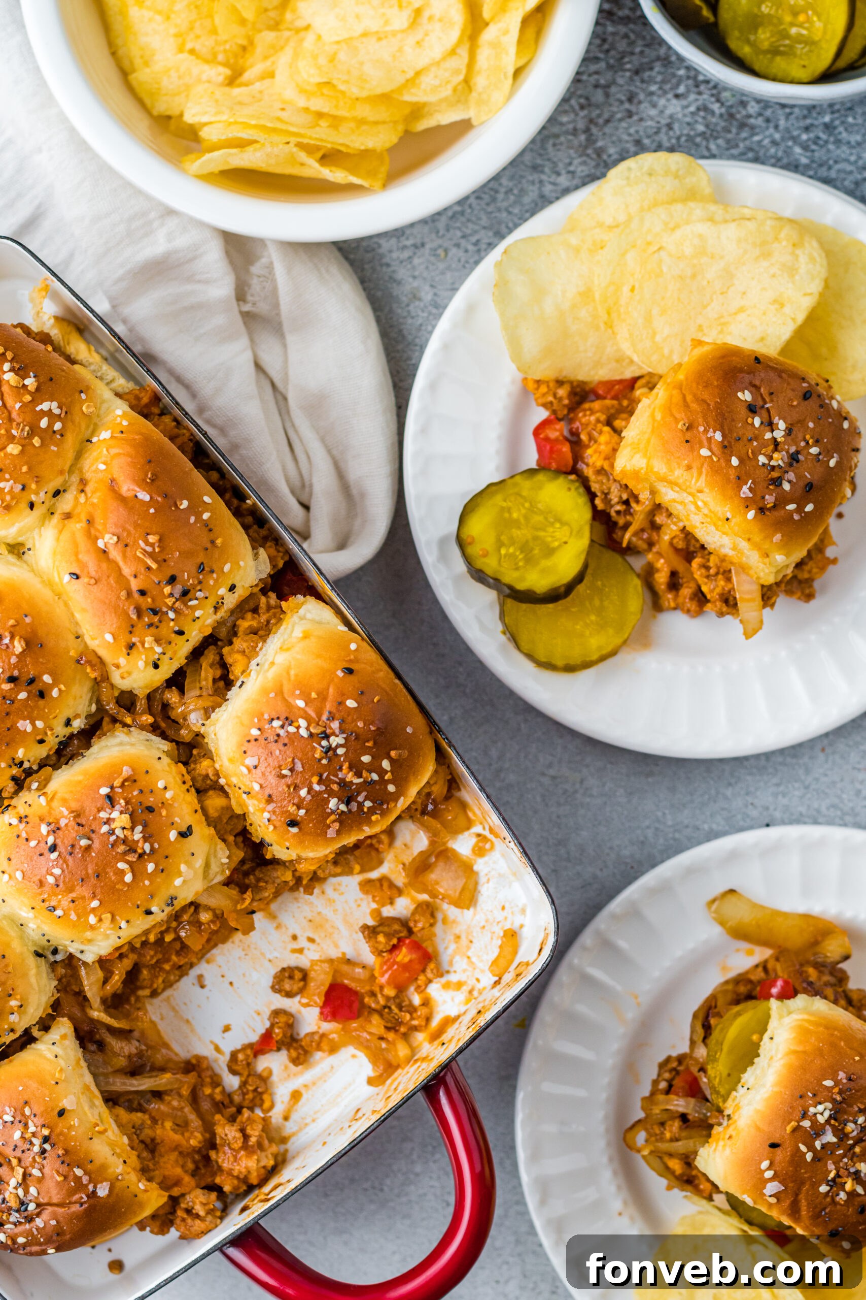 Overhead view of Cheesy Chicken Sloppy Joe Sliders on white plates served with pickle slices and chips, inviting and delicious.