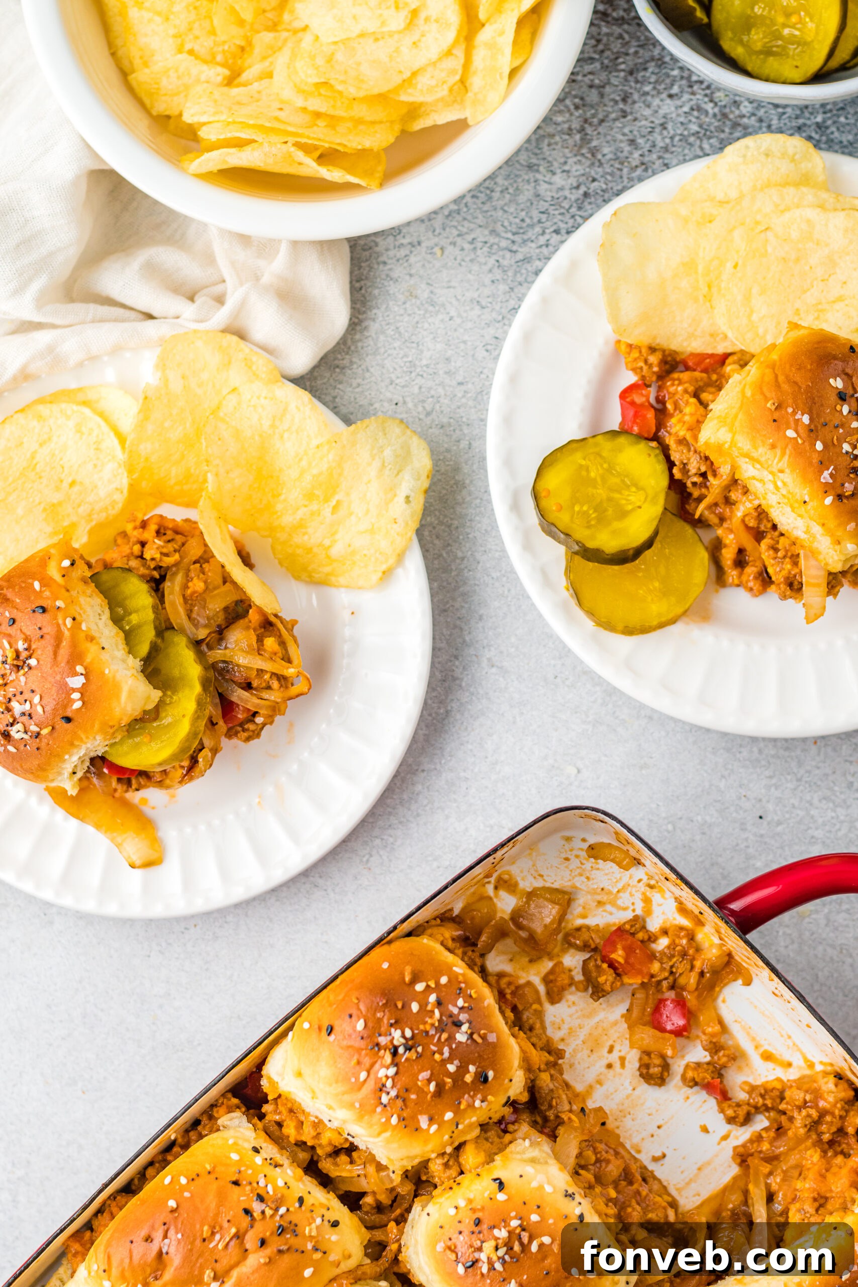 Overhead view of Cheesy Chicken Sloppy Joe Sliders on white plates served with pickle slices and chips, a perfect meal.