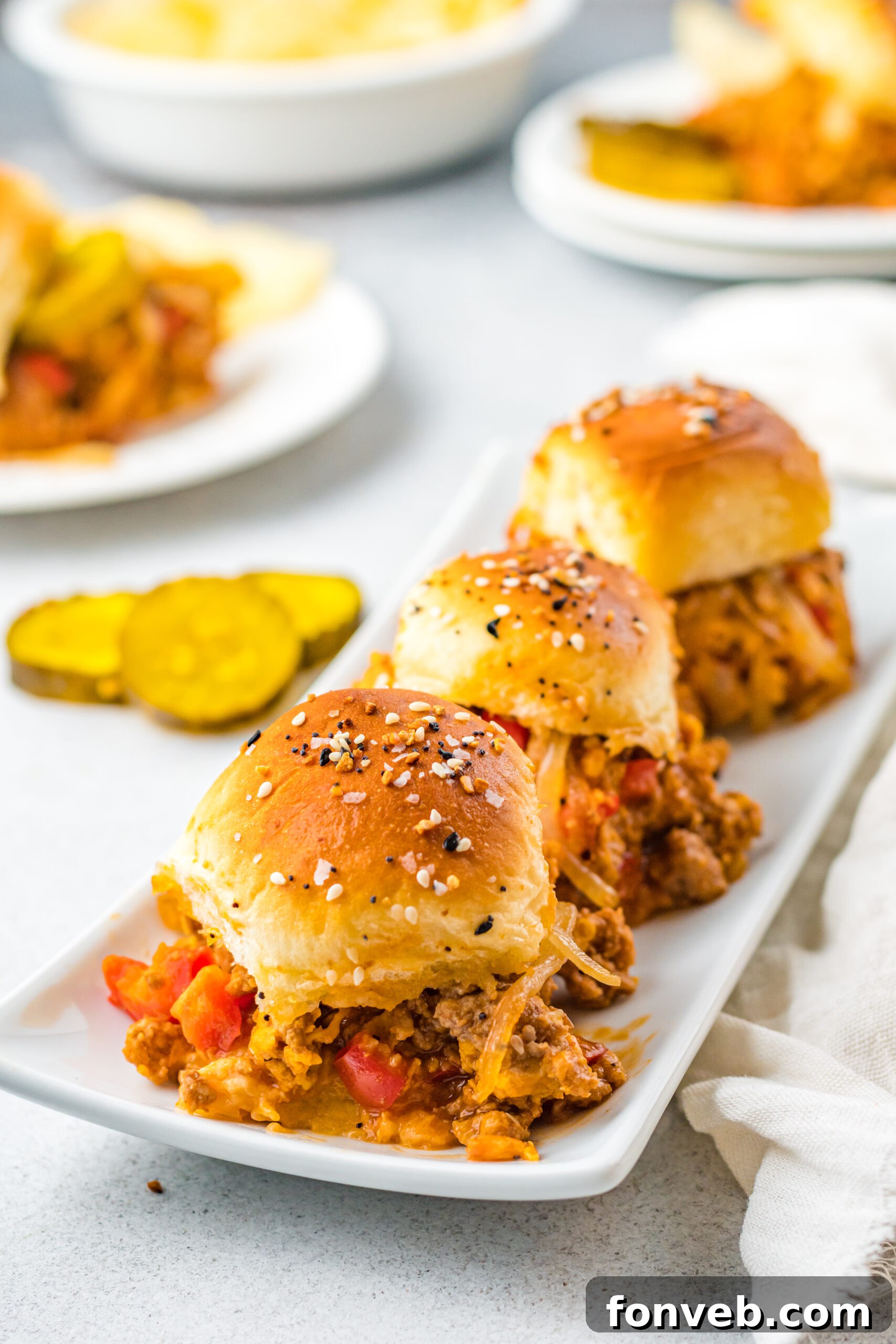 Front view of three Cheesy Chicken Sloppy Joe Sliders on a elegant white serving dish, perfectly golden and inviting.