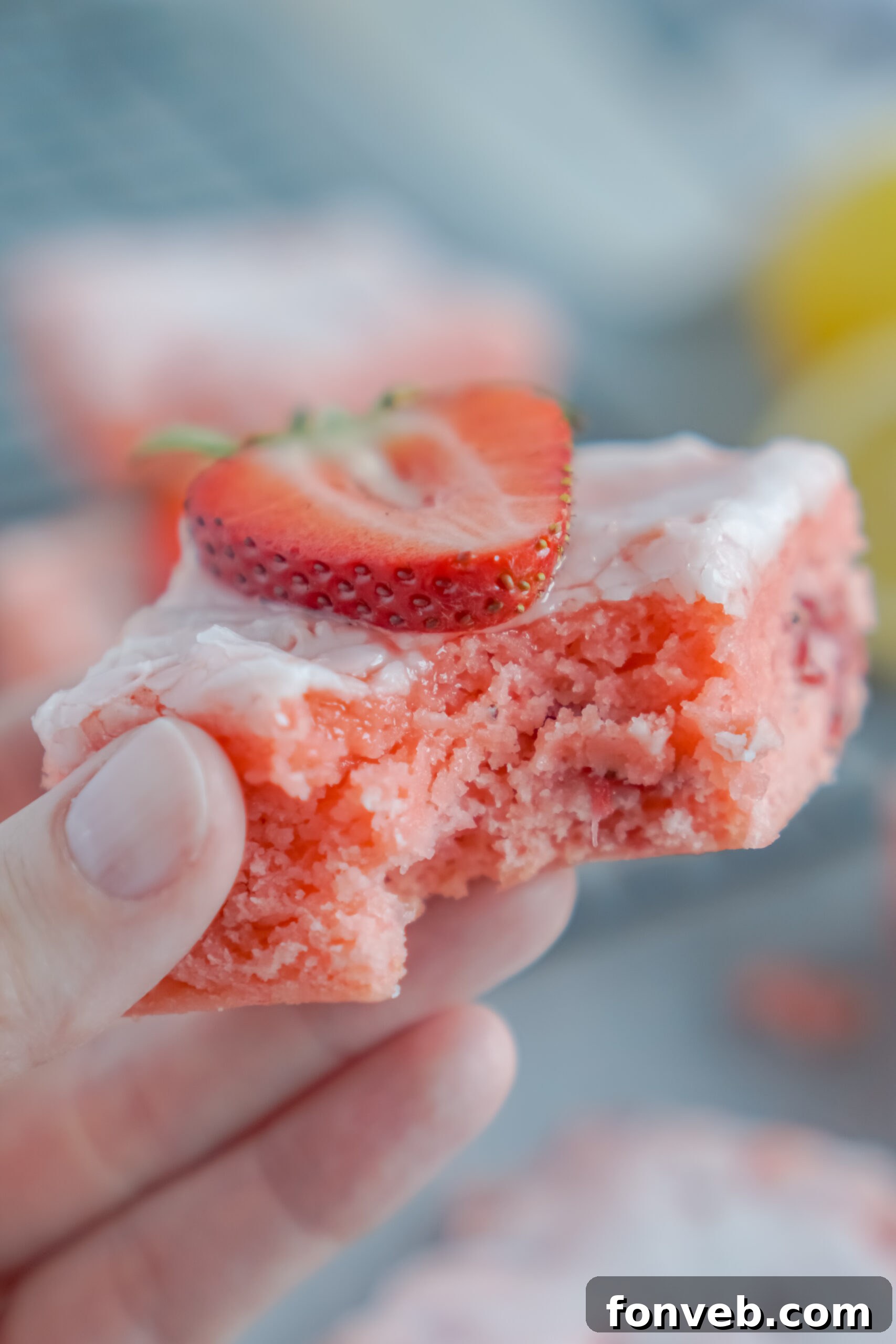 Hand holding a Strawberry Lemon Brownie with a bite taken out, highlighting its light color and moist interior.