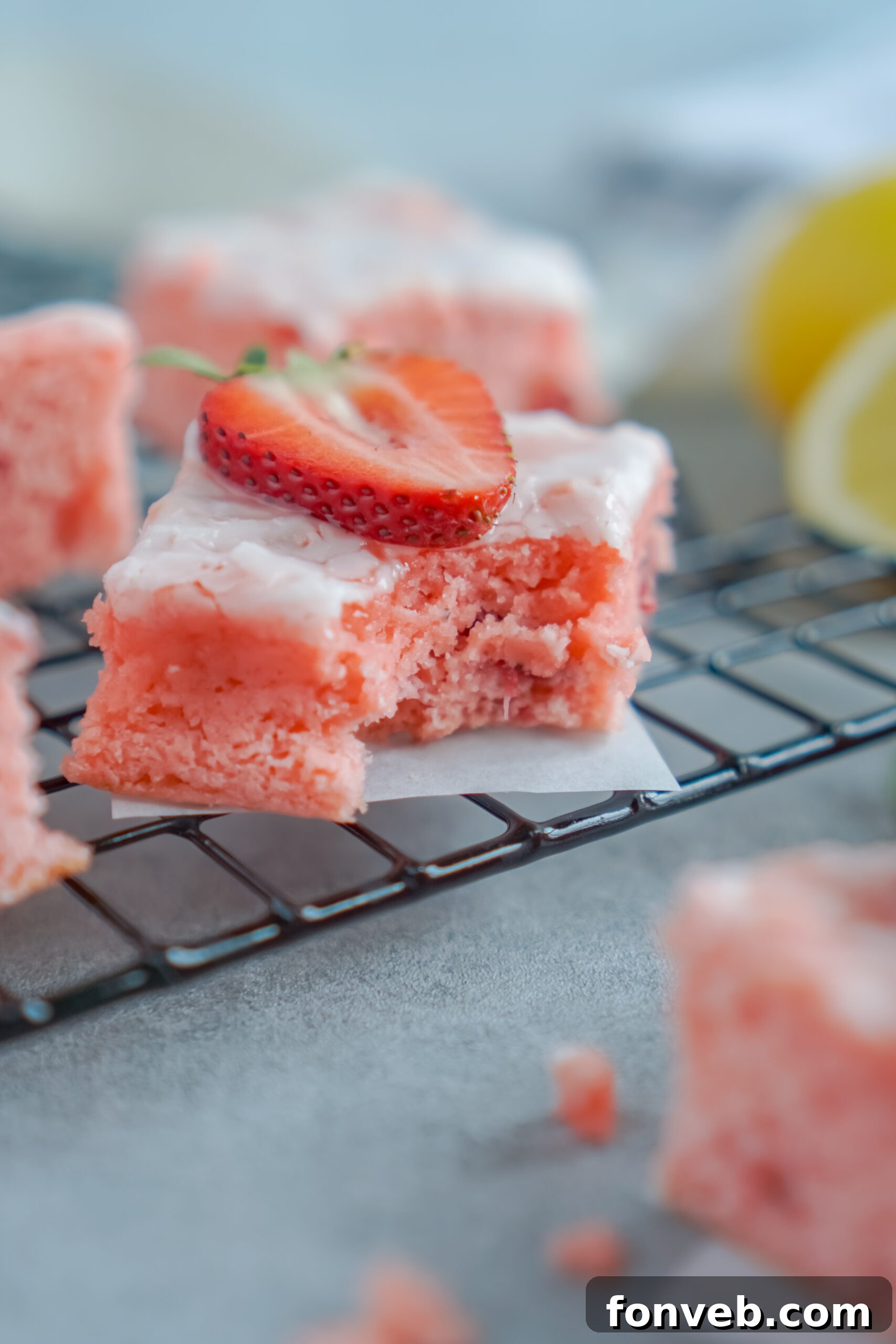 Single Strawberry Lemon Brownie on a black wire cooling rack with a corner bite removed, showing its soft texture.