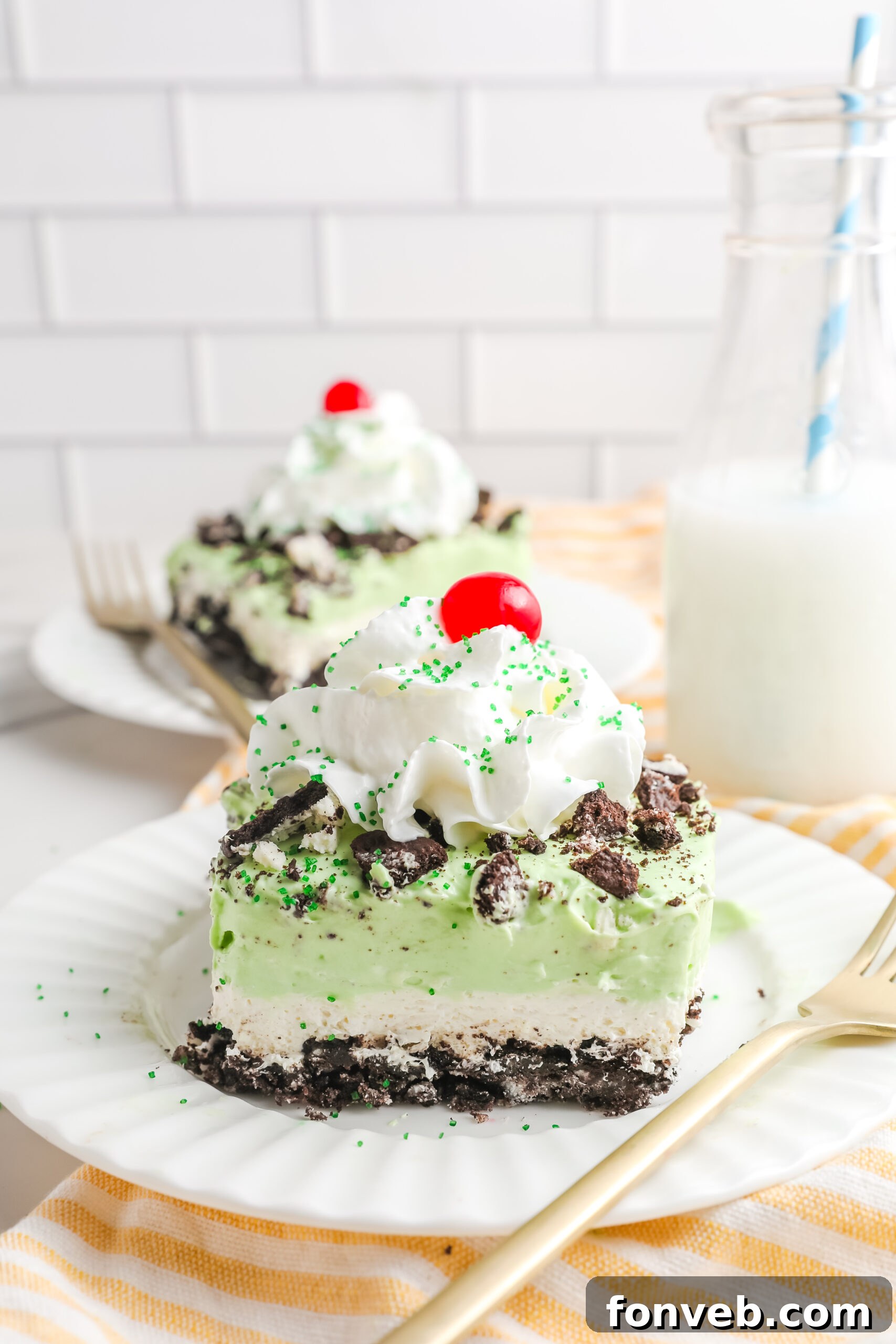 Emerald Lasagna 4 Two perfectly cut slices of Shamrock Lasagna dessert on elegant white plates, accompanied by gold forks, highlighting the distinct layers.