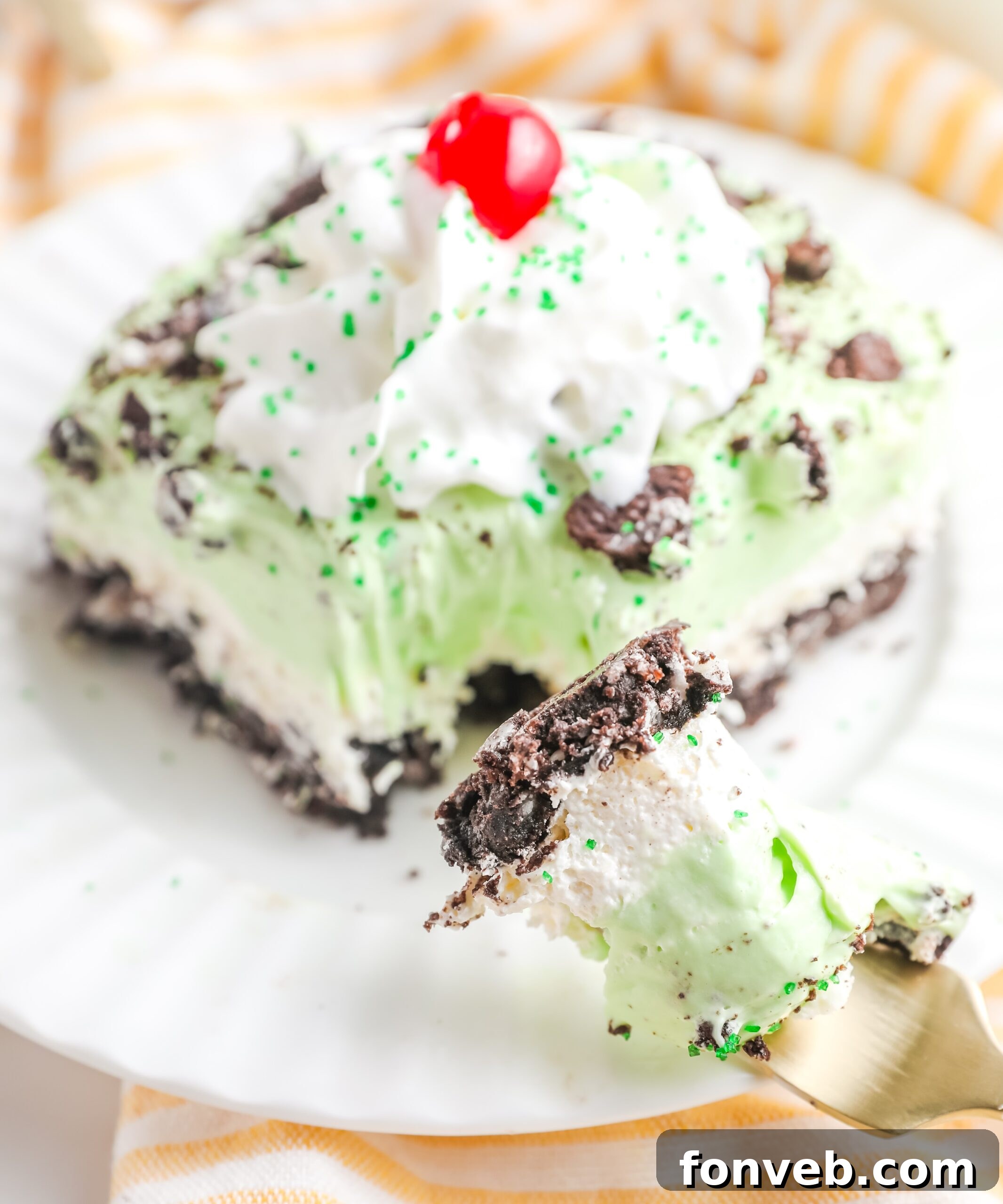 Emerald Lasagna 9 A side angle view of a slice of Shamrock Lasagna dessert, artfully topped with a dollop of whipped cream and a bright red maraschino cherry.