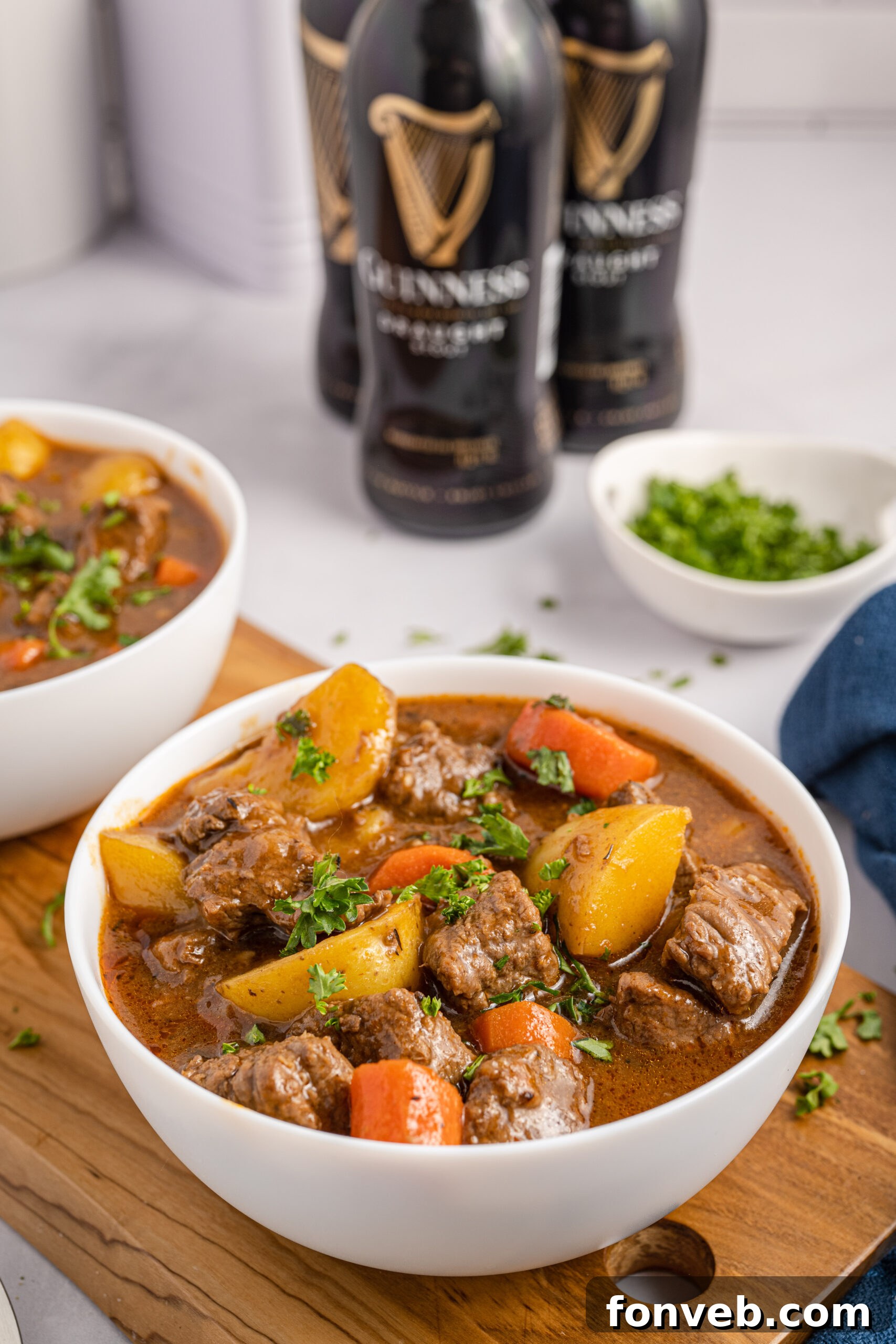 Two bowls of Irish stew sitting on a wooden board with Guinness beer bottles in the background. 