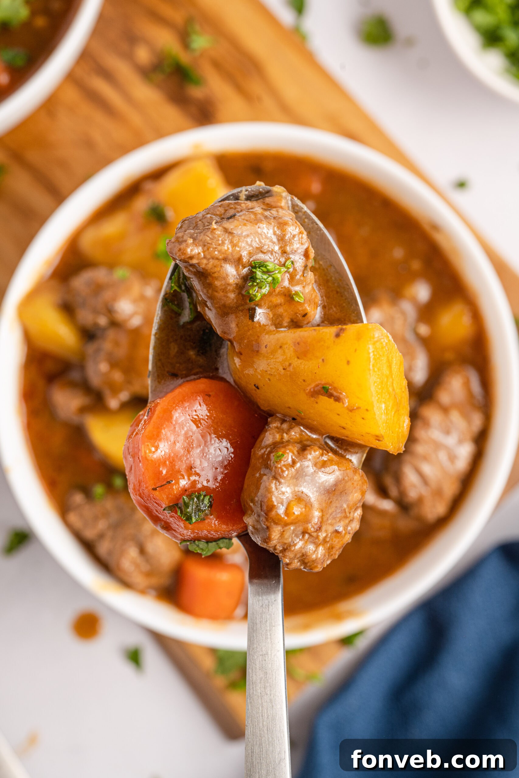 A silver spoon holding Irish Stew over a white bowl of stew. 