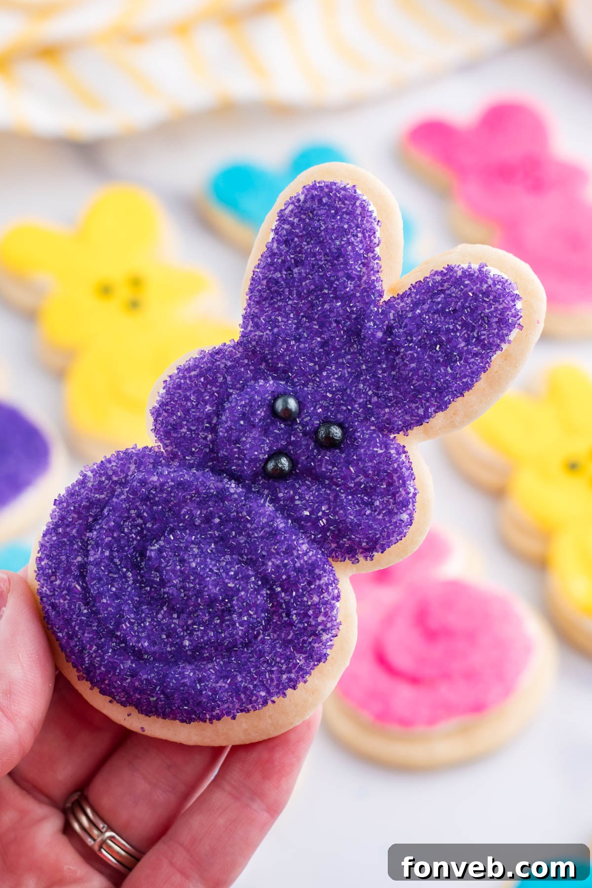 A hand holding up a vibrant purple Easter Bunny Cookie, showcasing its delightful color and adorable shape.