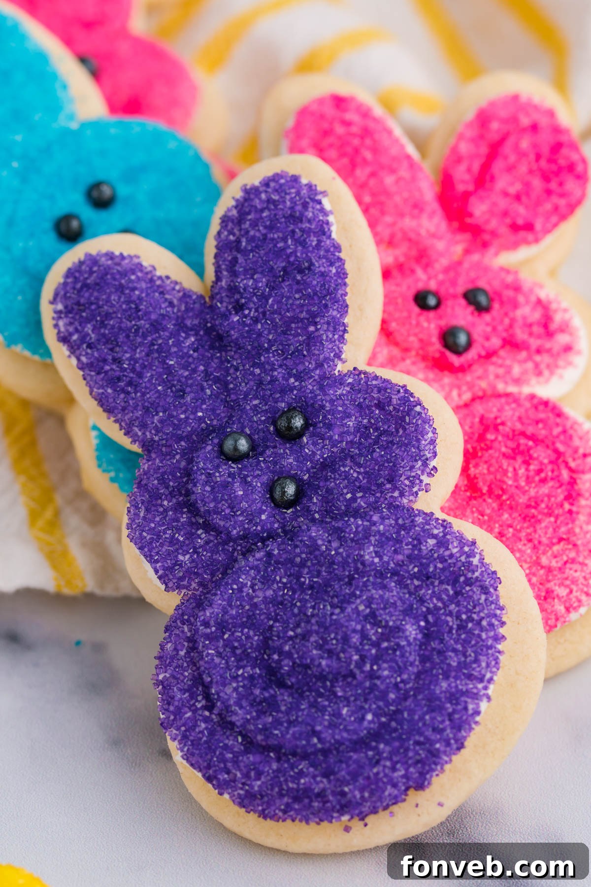 A charming stack of multicolored Easter Bunny Cookies, artfully arranged on a white and yellow linen, perfect for a festive display.