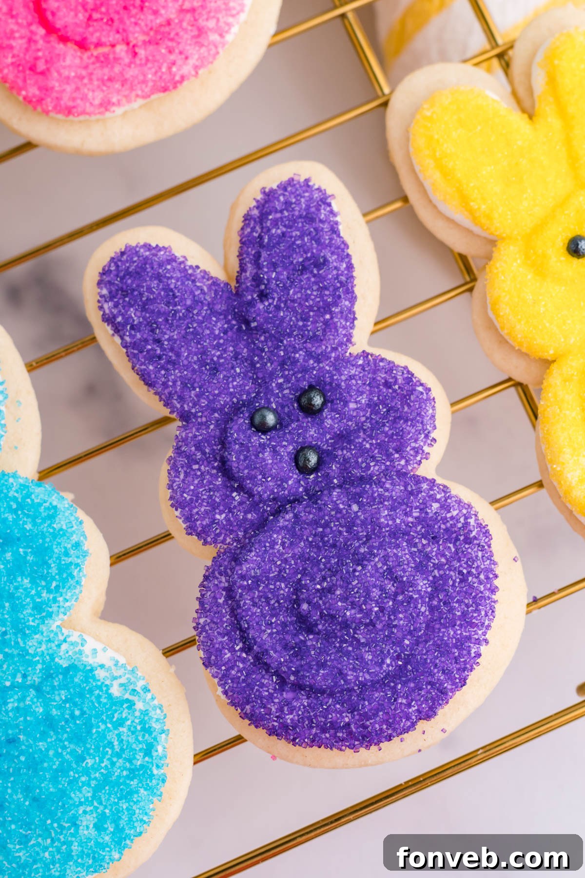 A close-up, overhead view of a perfectly frosted purple bunny cookie resting on a gold cooling rack, awaiting its festive moment.
