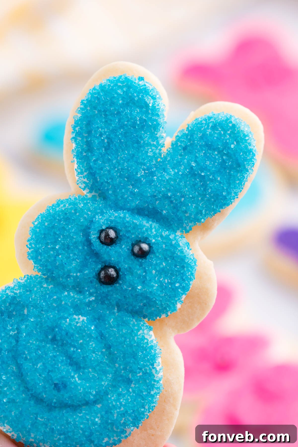 A hand gently holding a vibrant blue Easter Bunny Cookie, showcasing its smooth frosting and cheerful appearance.