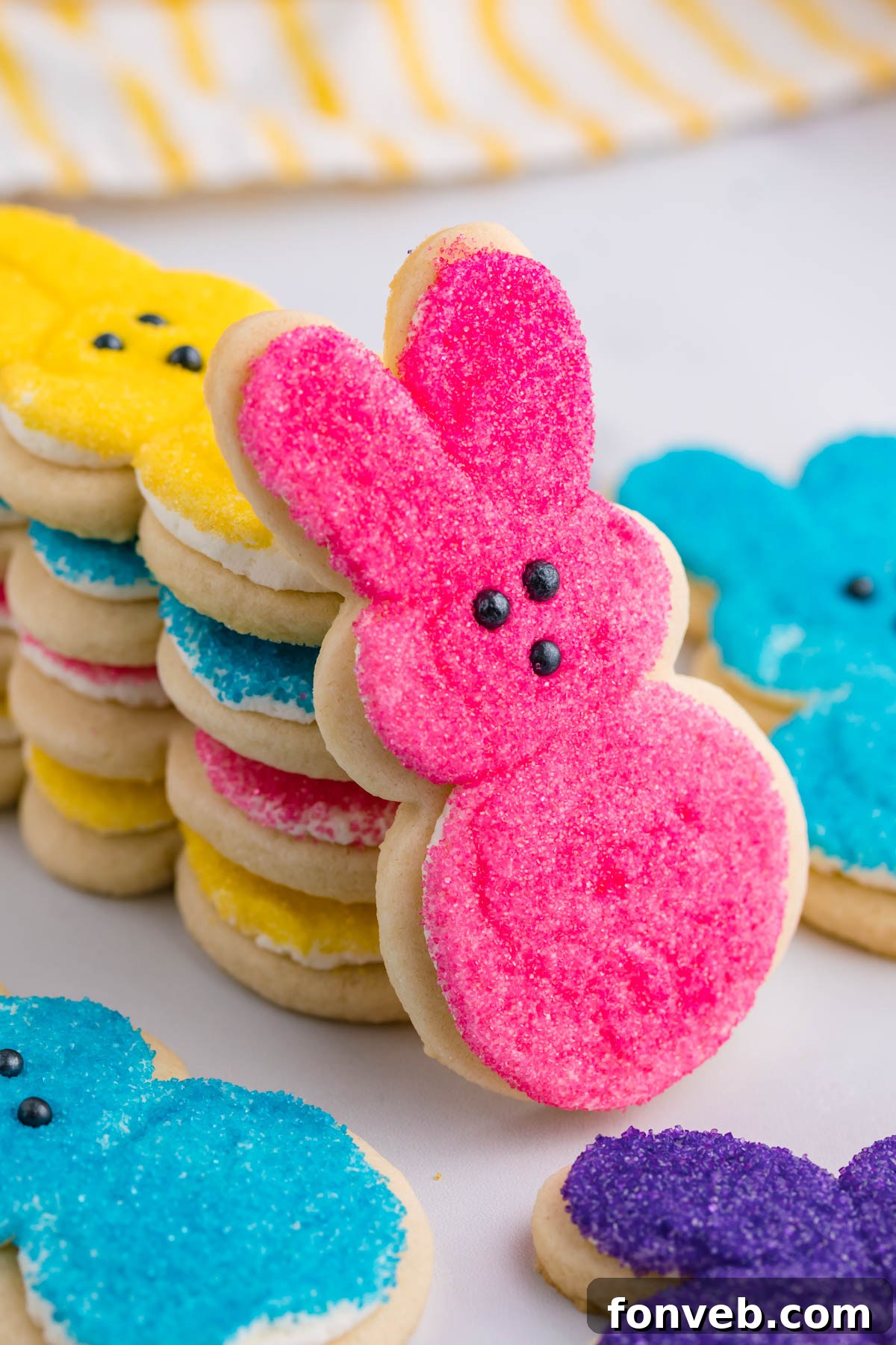 A cheerful pink Bunny Cookie, perfectly frosted, propped up against a stack of various multicolored Easter Bunny Cookies.