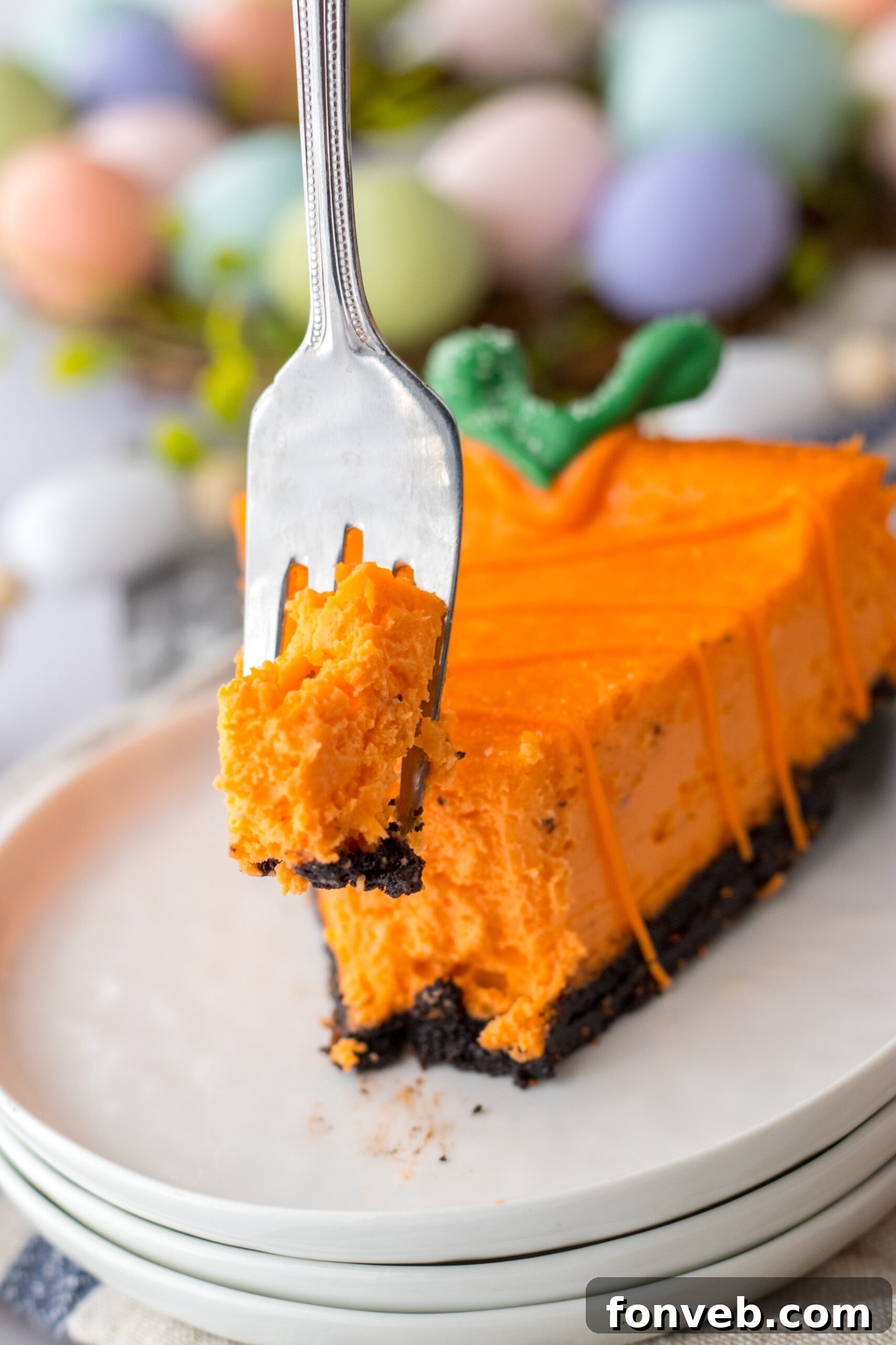 A single cheesecake carrot is showcased on a white plate, with a silver fork gracefully taking a portion, highlighting its tempting layers.