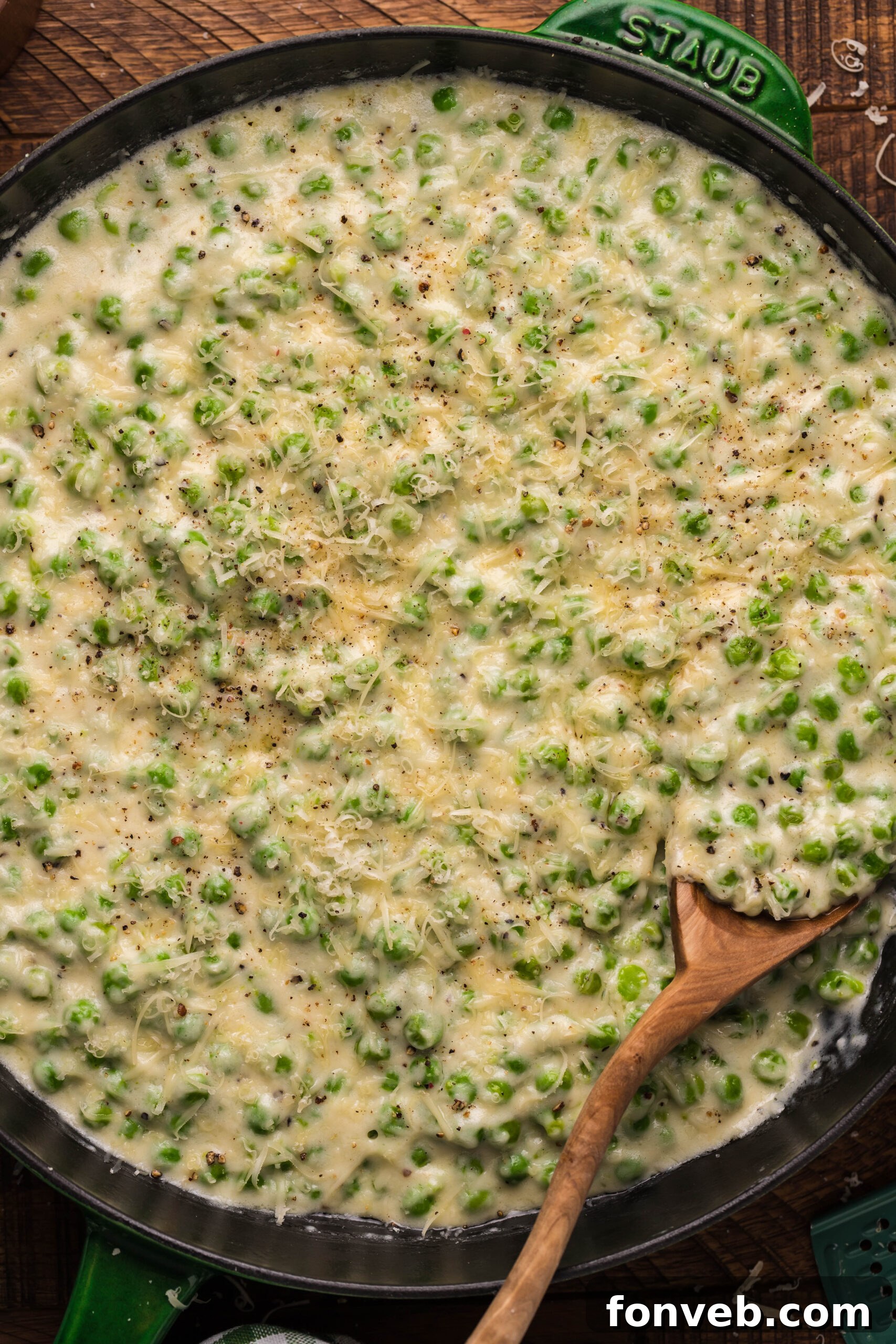 Close up shot of creamed peas in a green and black cast iron skillet with a wooden spoon. 