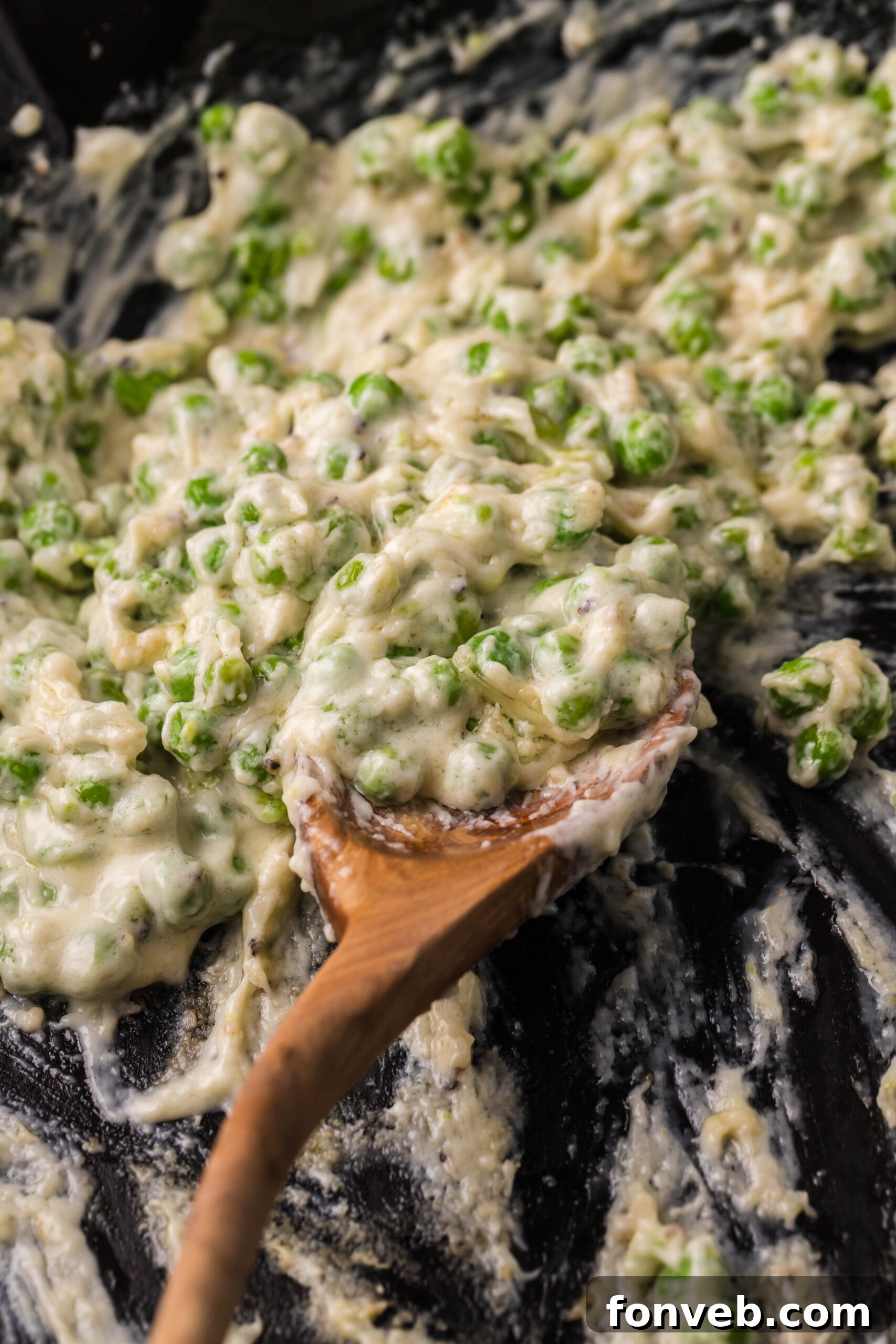 A wooden spoon removing creamed peas from a cast iron skillet. 
