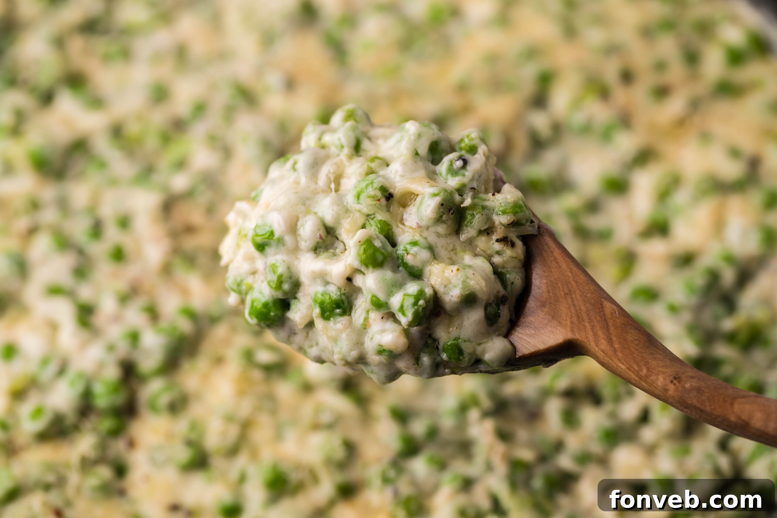 A wooden spoon removing creamed peas from a cast iron skillet. 