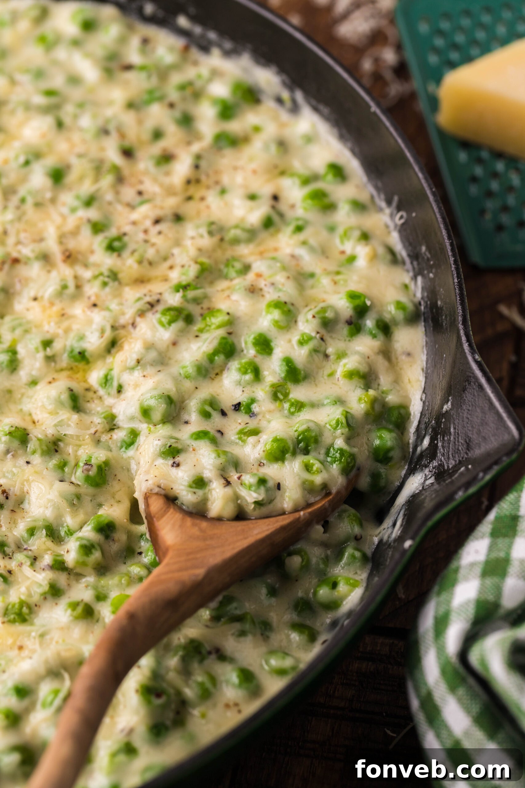 Close up shot of Creamed Peas in a black and green cast iron skillet with a wood spoon. 