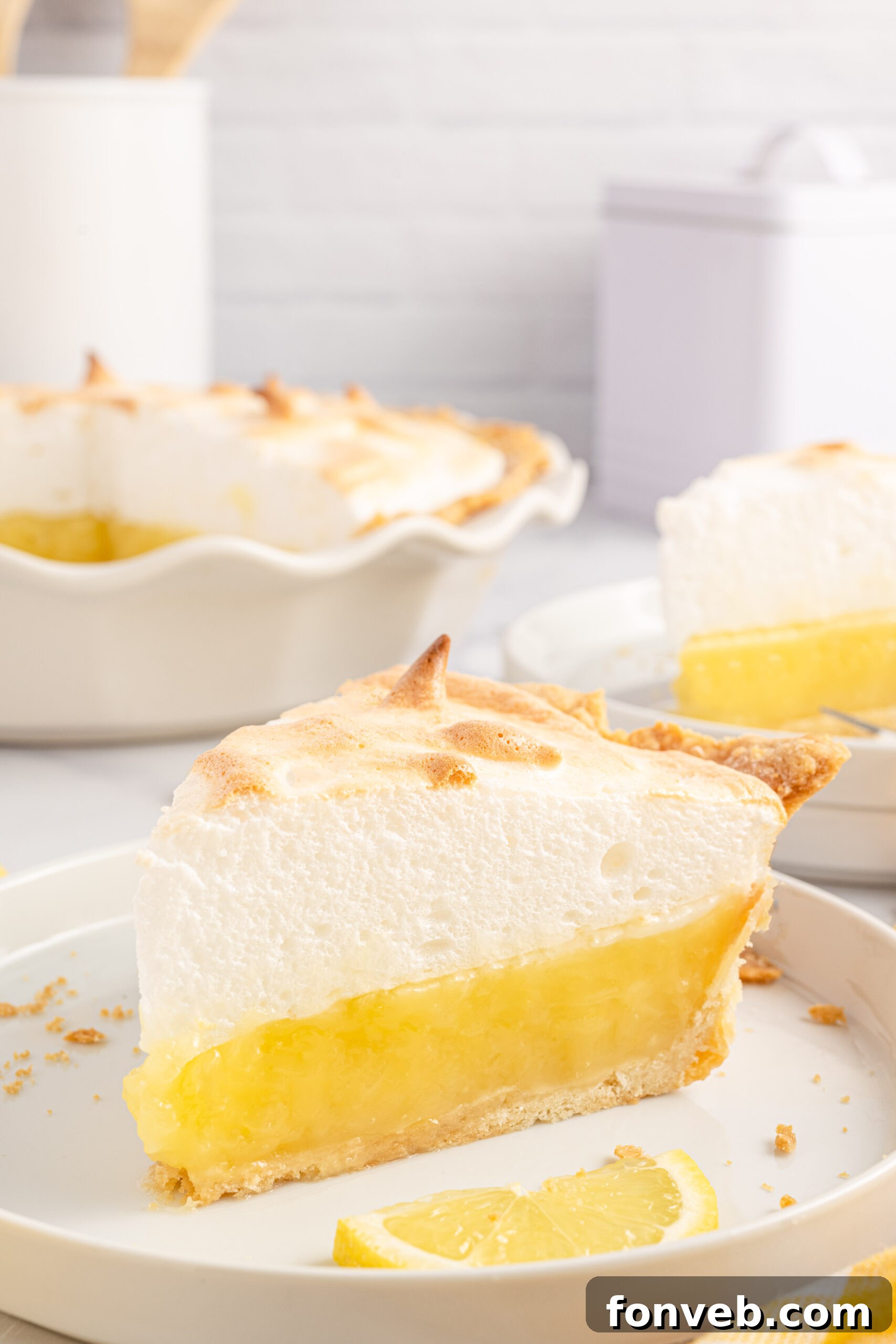 up close view of a piece of the lemon meringue pie on a white plate with fresh sliced lemons. 