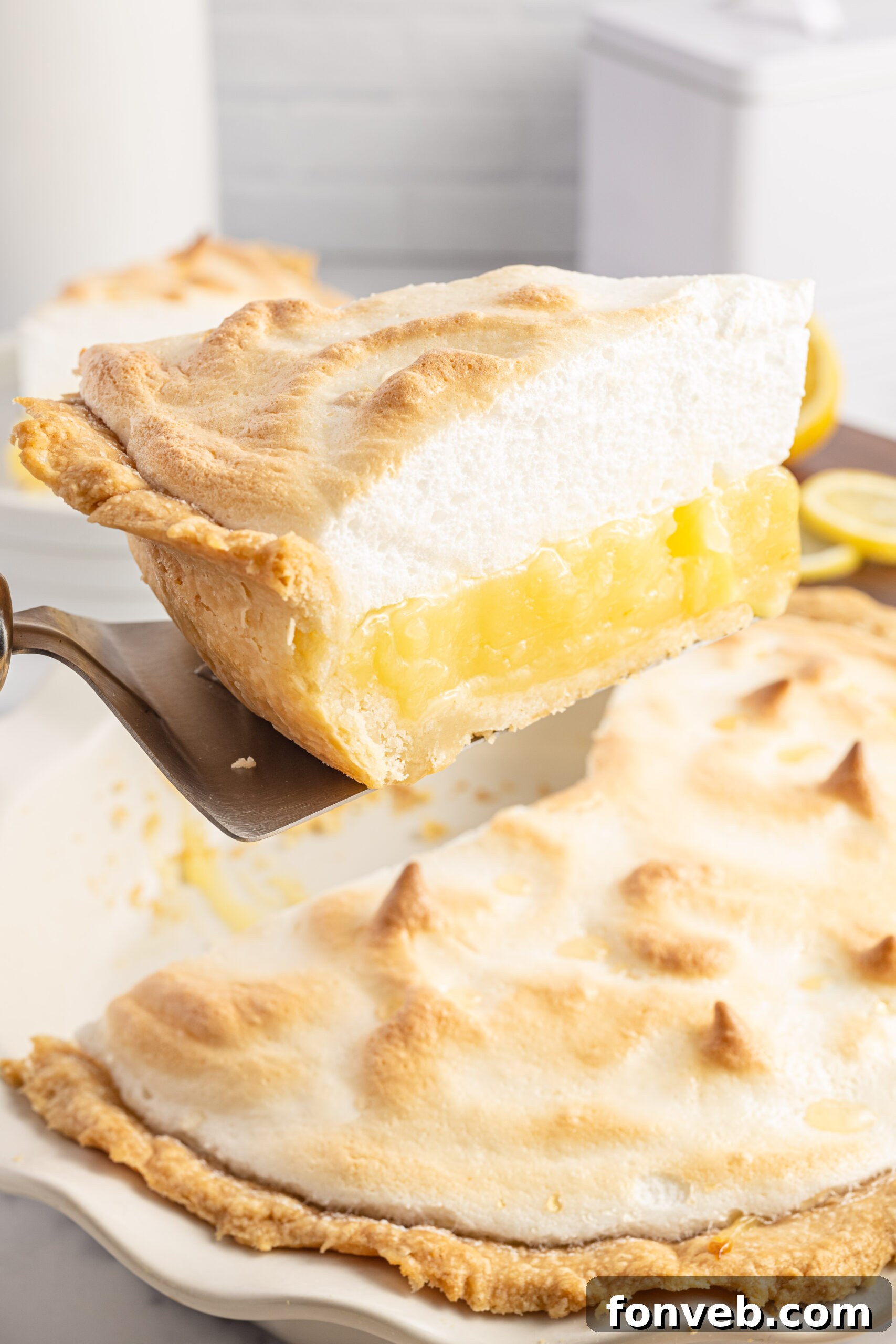 A slice of lemon pie being held up by a silver spatula. 