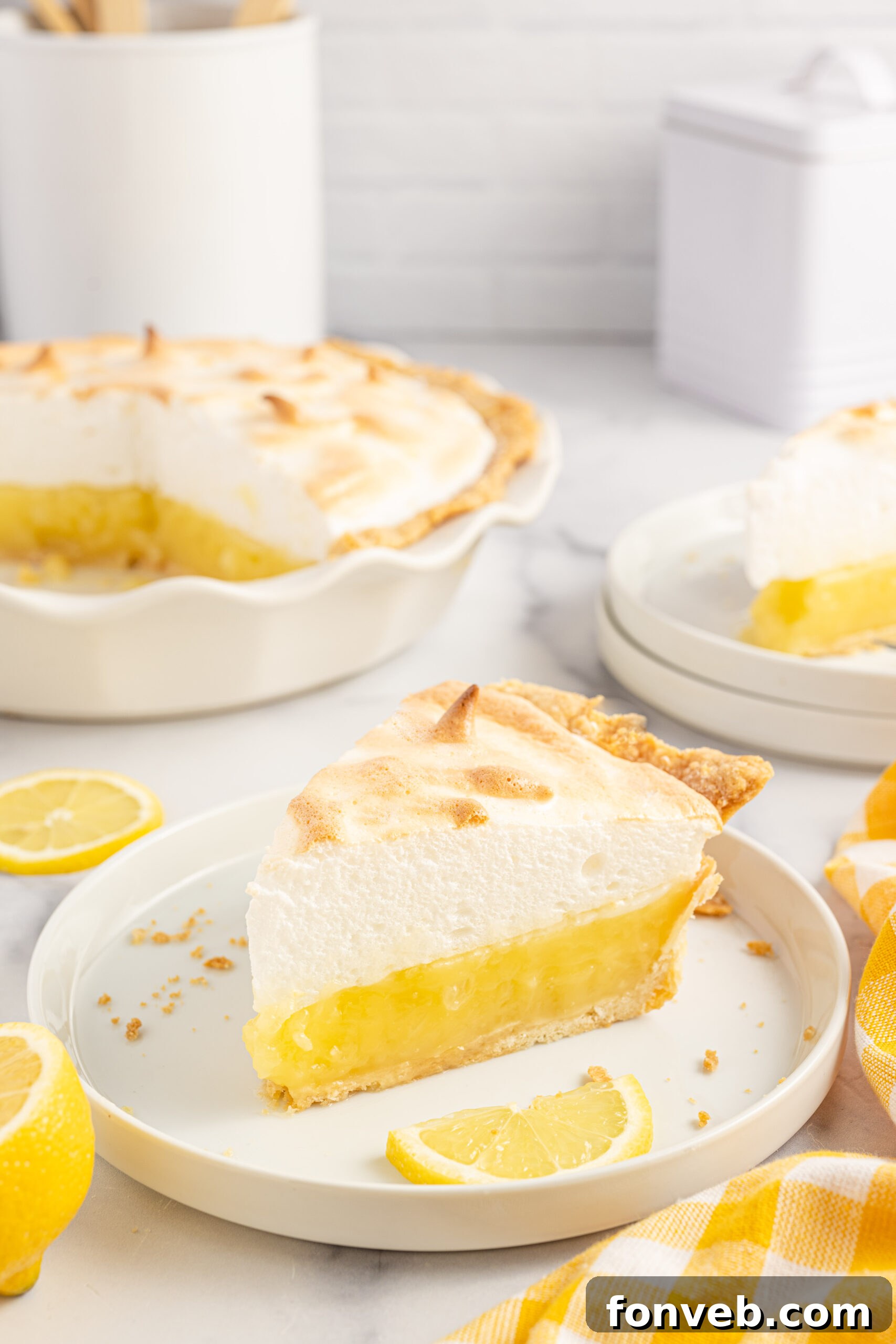 A piece of meringue pie on a white plate with fresh lemons. 