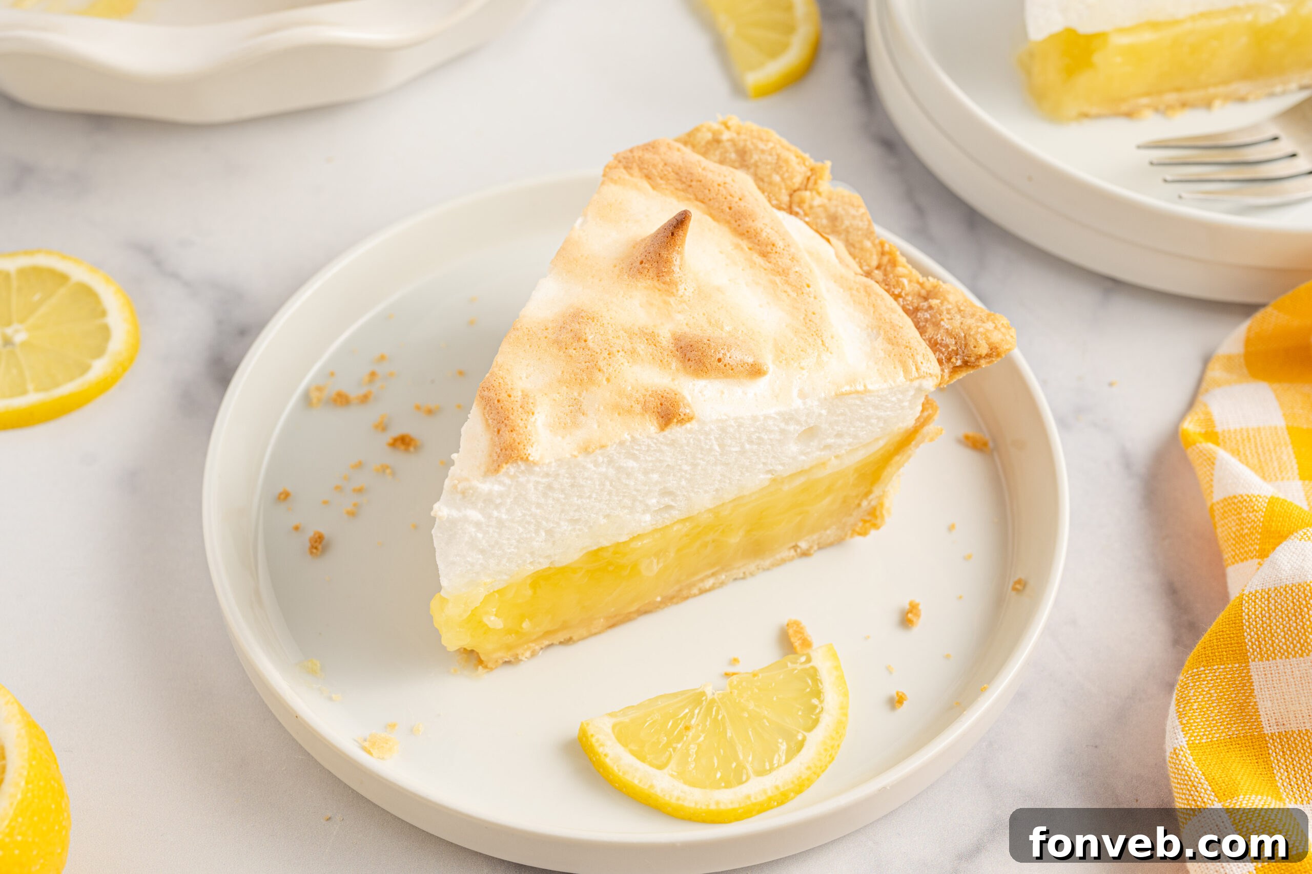 A piece of meringue pie on a white plate with fresh lemons. 