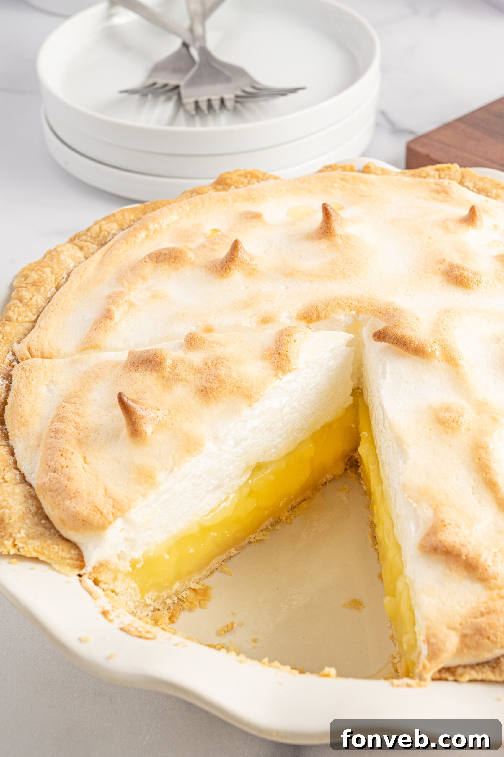 Side shot of a slice of lemon meringue pie in a white pie dish. 