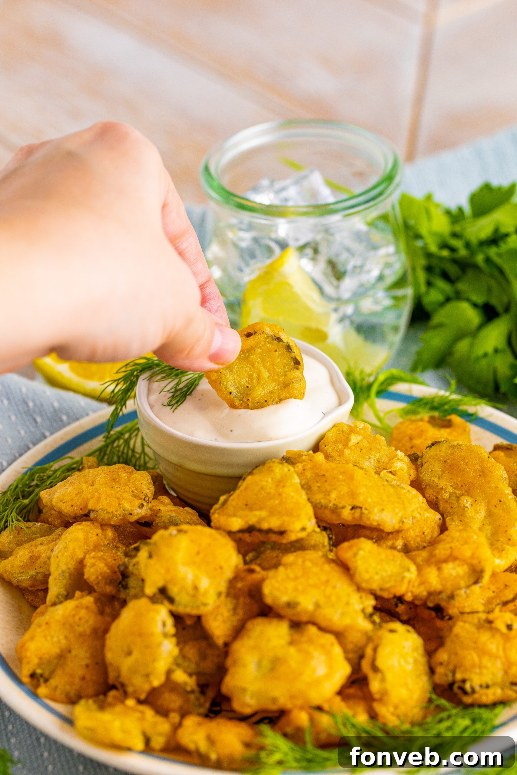 A hand dipping a fried pickle into ranch sauce. 