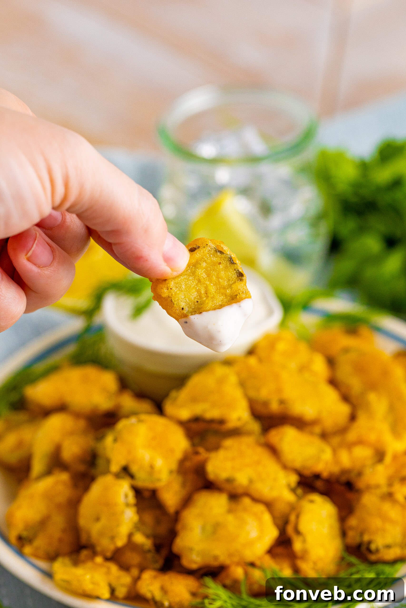 A hand holding a fried pickle that has been dipped in ranch sauce. 