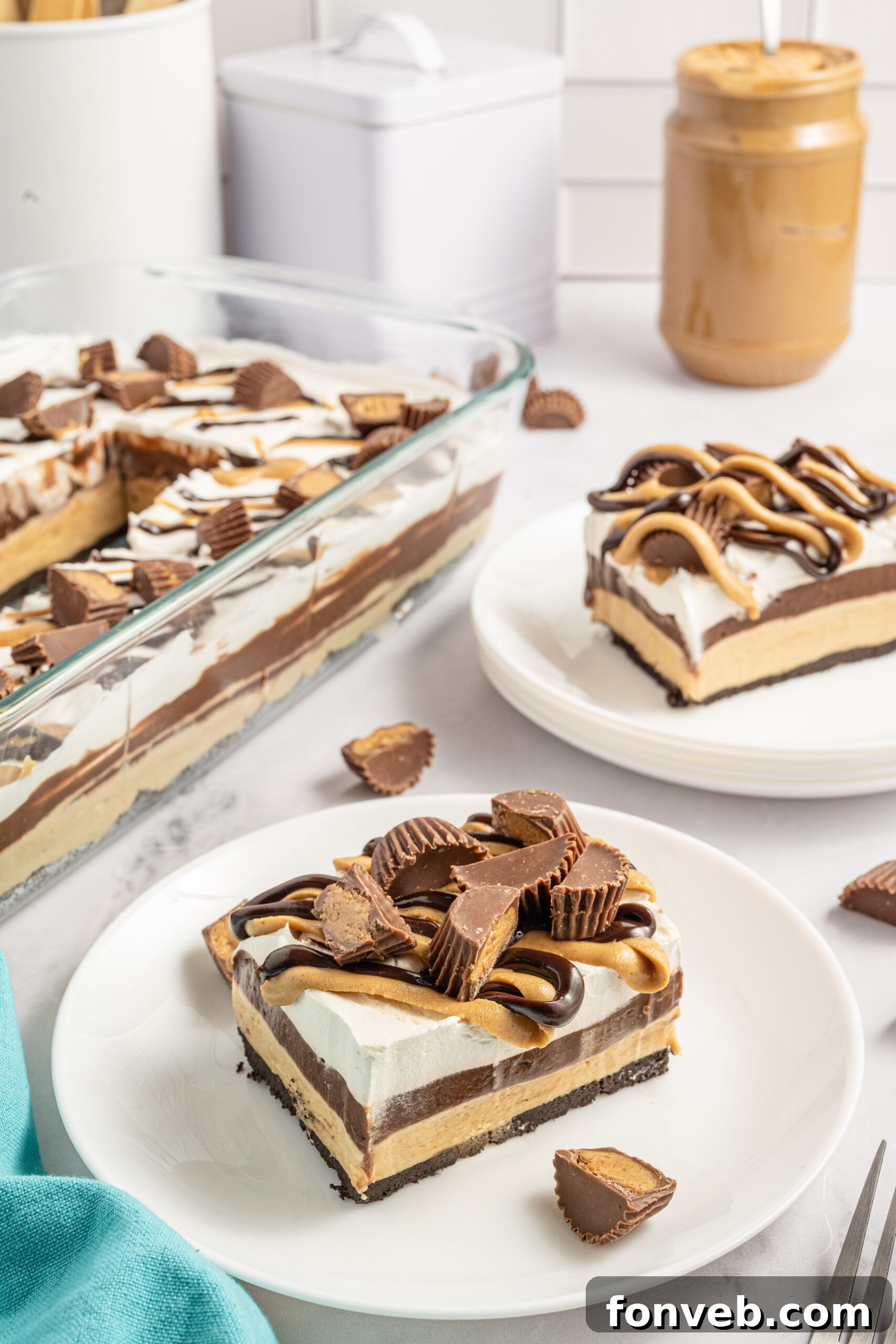 Reese's Peanut Butter Cup Lasagna 13 Two enticing slices of chocolate peanut butter lasagna presented on pristine white plates, with a scattering of Reese's Peanut Butter Cups in the background, hinting at the dessert's inspiration.