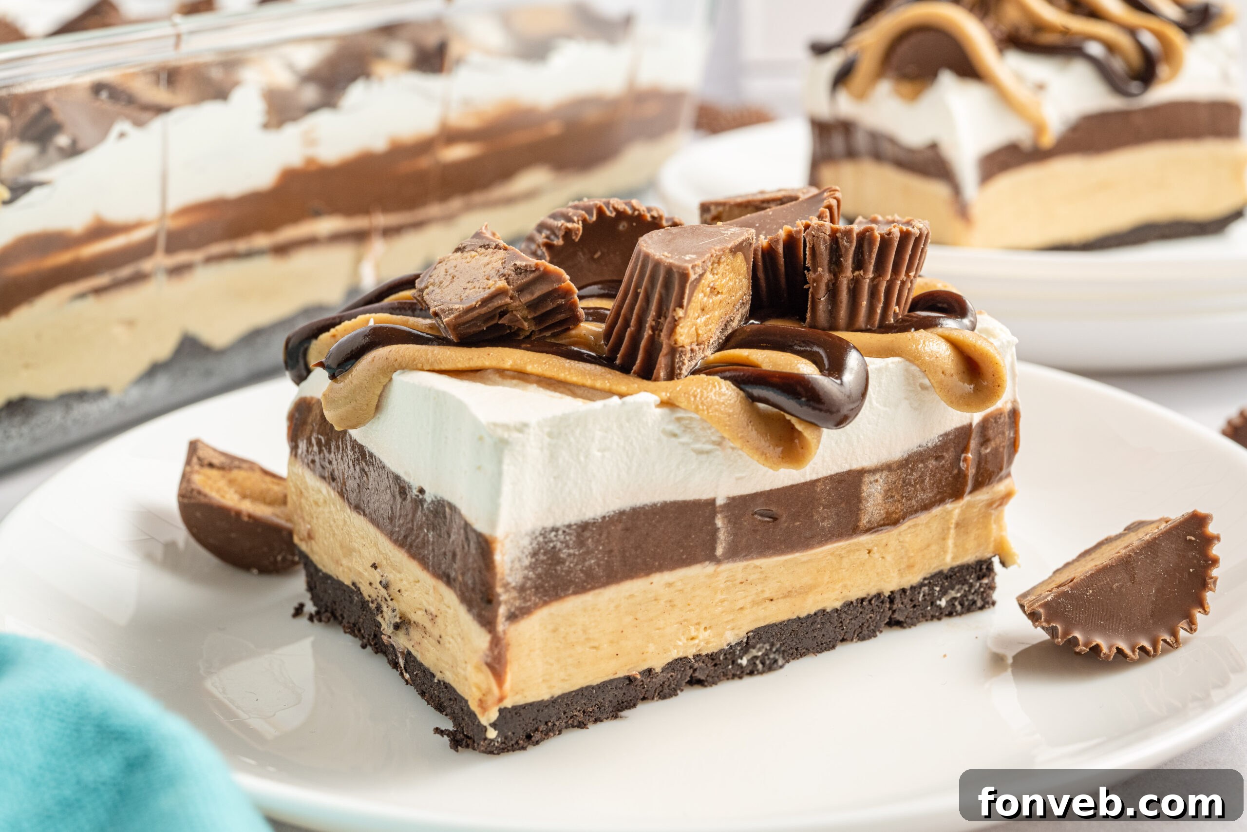 Reese's Peanut Butter Cup Lasagna 14 A single, perfectly portioned slice of chocolate peanut butter lasagna on a white plate, with more Reese's Peanut Butter Cups in the background.