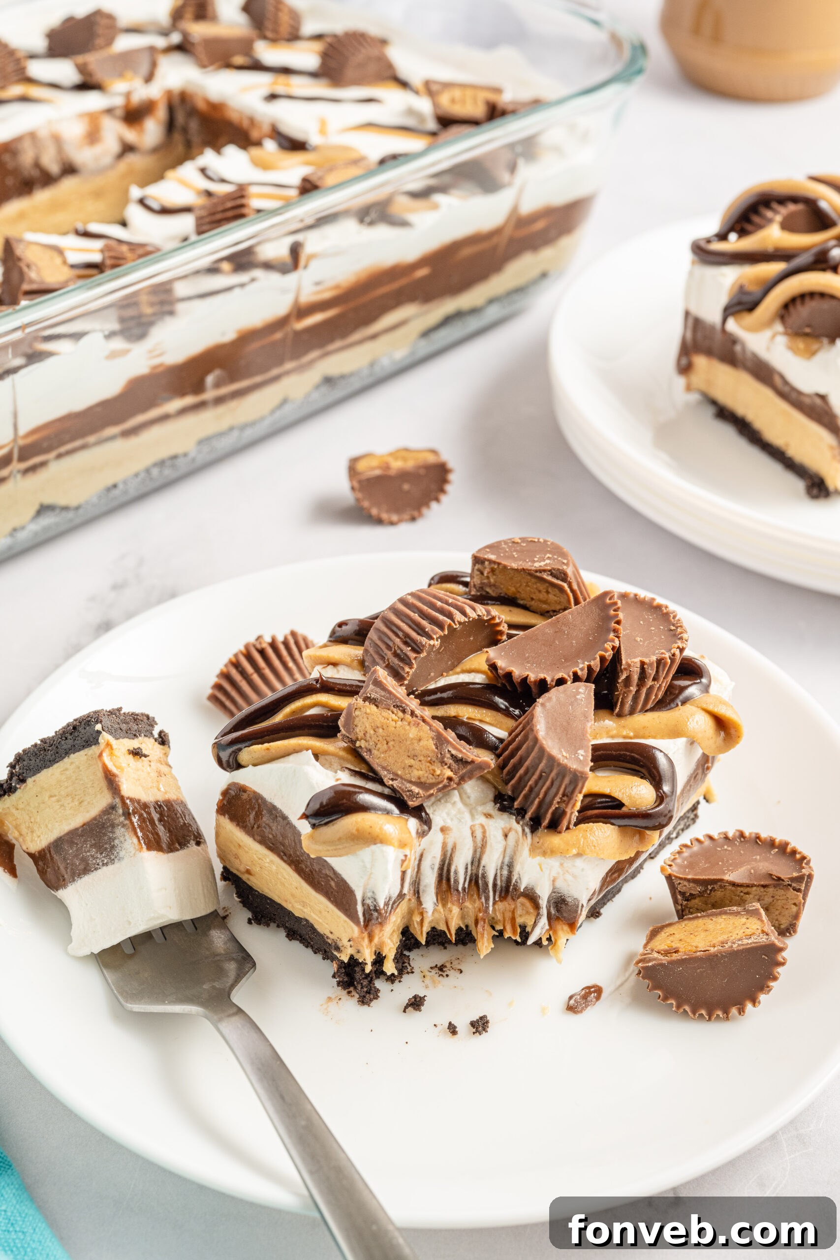 Reese's Peanut Butter Cup Lasagna 17 Two perfectly arranged pieces of chocolate peanut butter lasagna on white plates, with Reese's Peanut Butter Cups scattered in the background, creating an inviting scene.