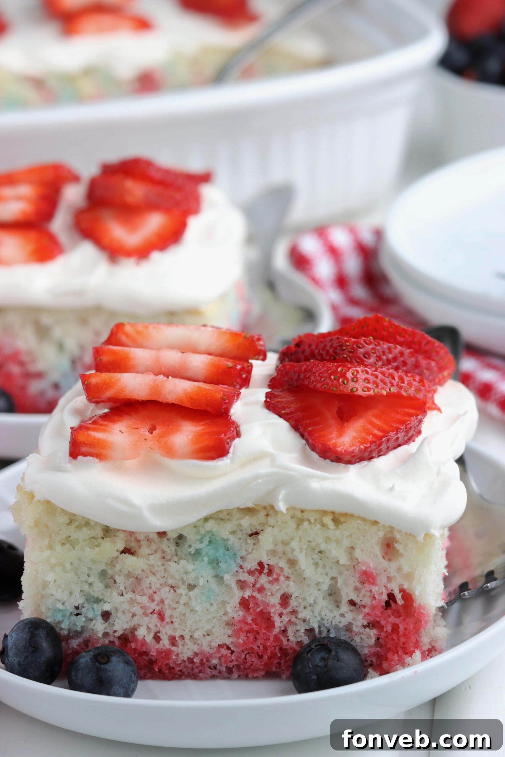 A slice of American Flag Cake, showing the distinct red, white, and blue colors, on a white plate with berries.