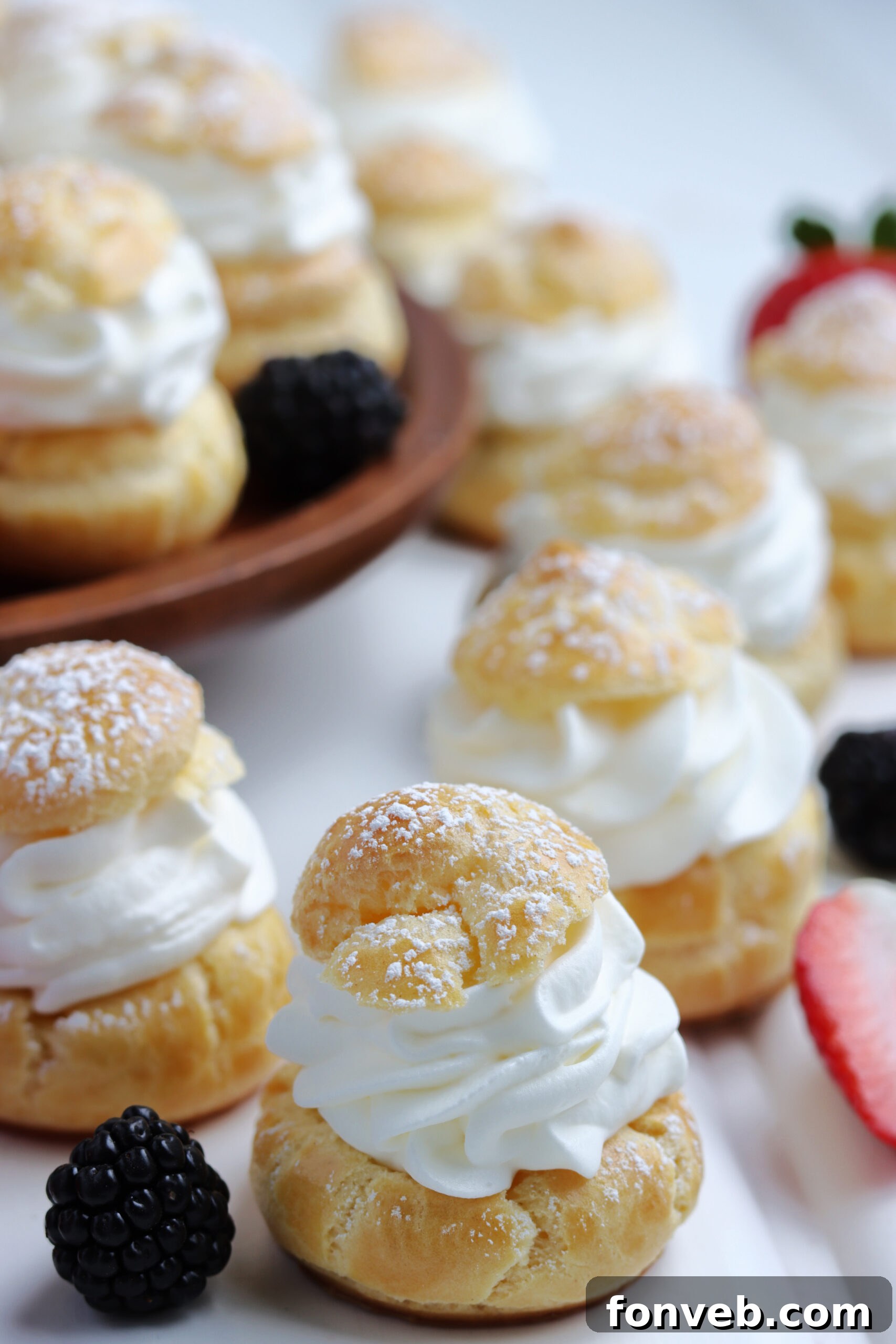 Cream puffs sprinkled with powdered sugar and fresh berries in the background, showcasing their delicate appearance.