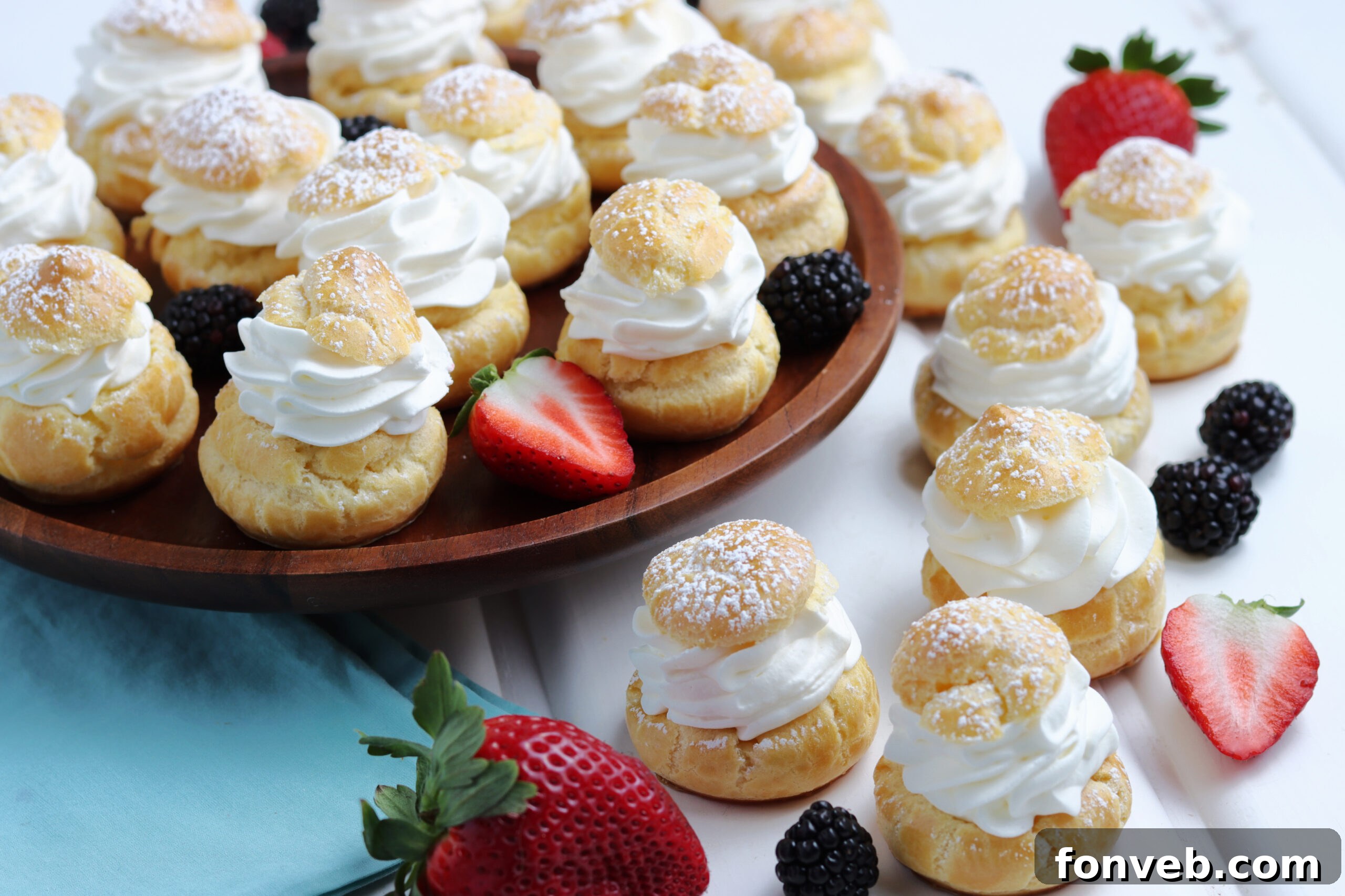 Overhead shot of cream puffs generously sprinkled with powdered sugar, accompanied by fresh berries, artfully arranged on a serving tray.