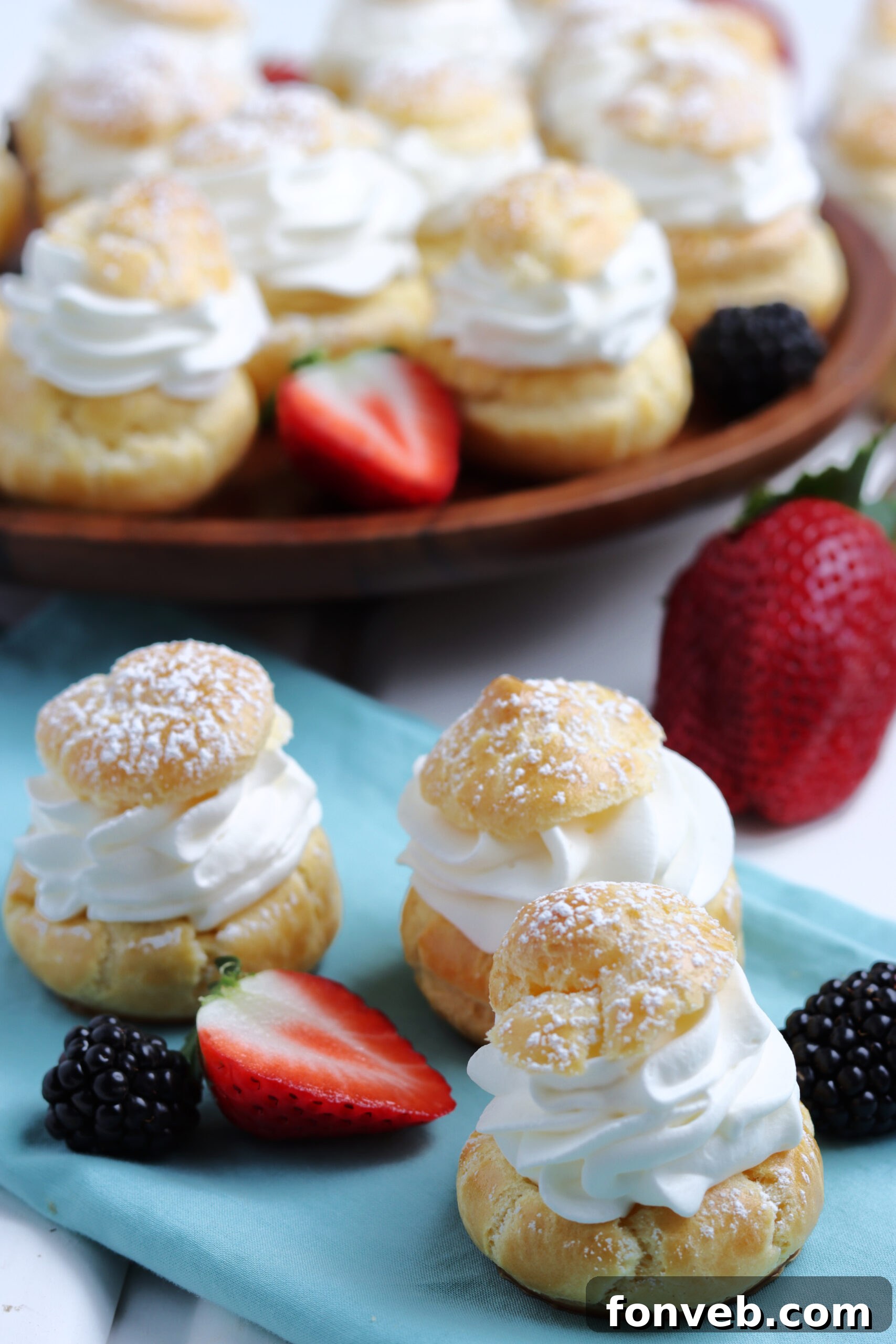 Three perfectly formed cream puffs, dusted with powdered sugar, sitting alongside a scattering of fresh berries.