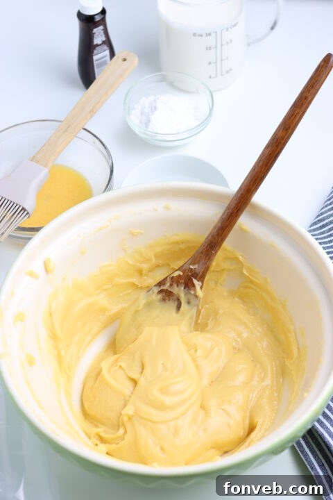 A hand mixing the choux pastry dough in a saucepan on the stove, showing the critical stage of drying the dough.