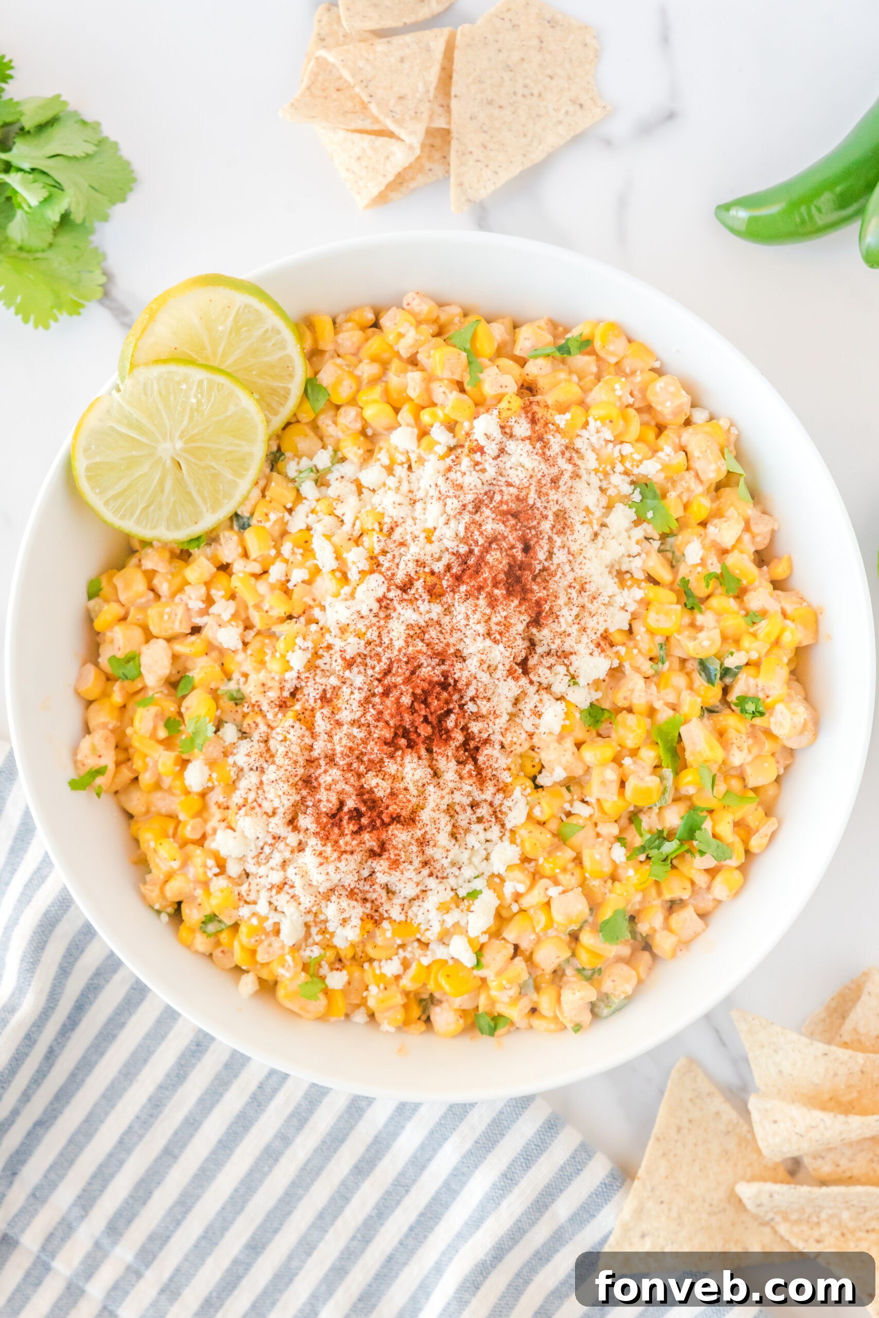 A large white bowl brimming with Mexican Street Corn Salad, garnished with a sprinkle of paprika and fresh lime slices, ready to be served.