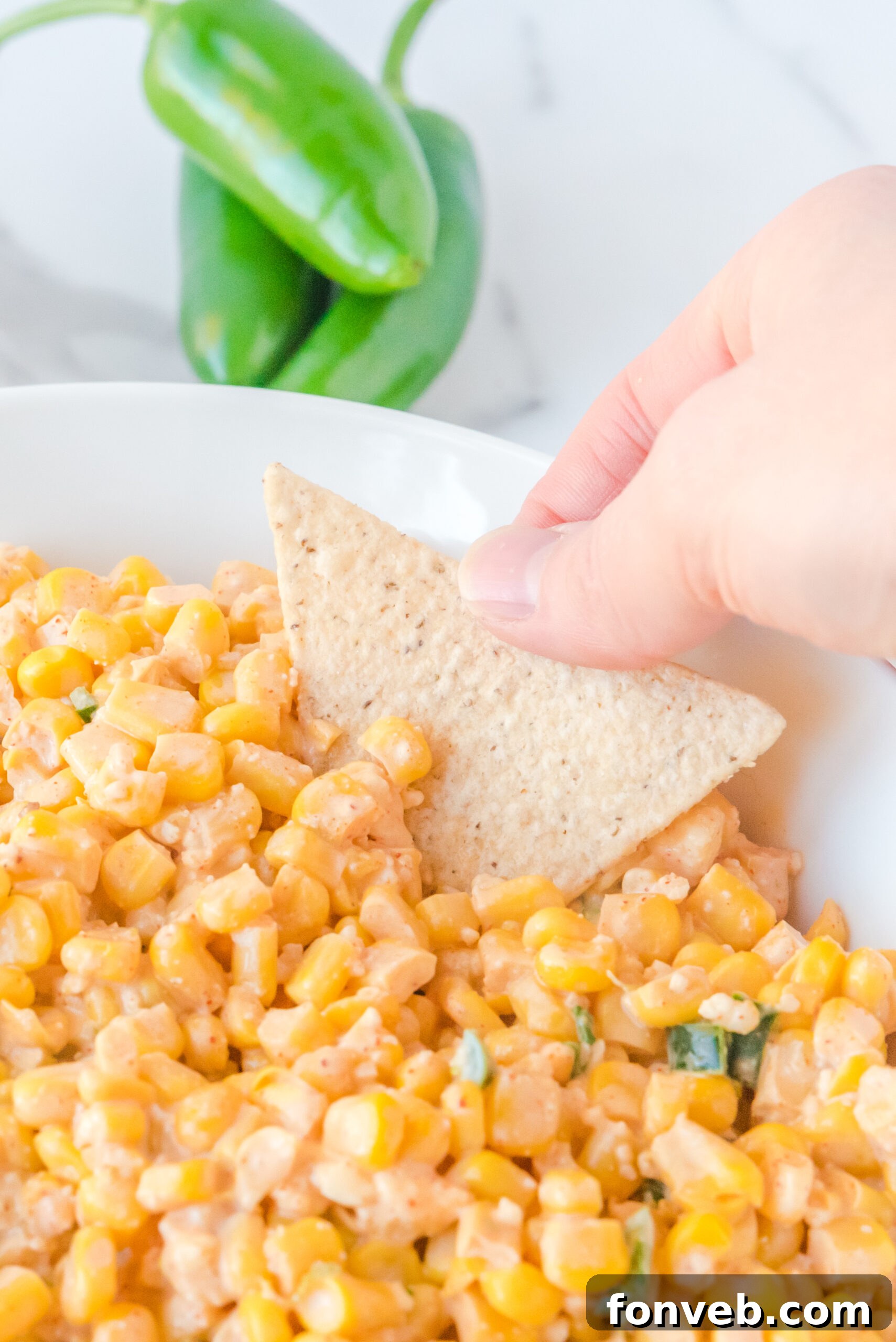 A tortilla chip being dipped into the rich and creamy Mexican Street Corn Salad, showcasing its inviting texture and readiness to be enjoyed.