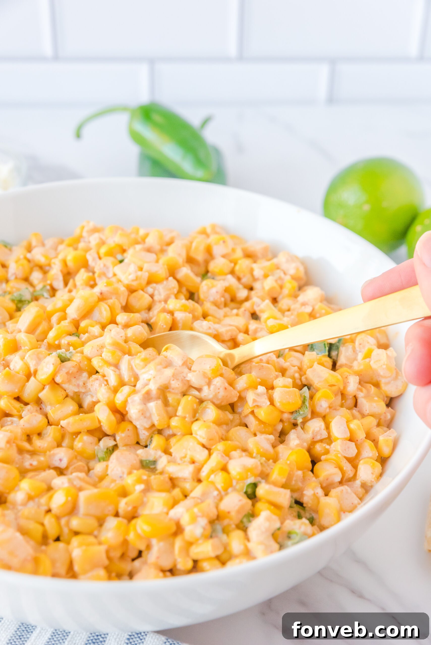 A gold-colored spoon carefully scooping a generous portion of Mexican Street Corn Salad from a large white serving bowl, highlighting its texture.