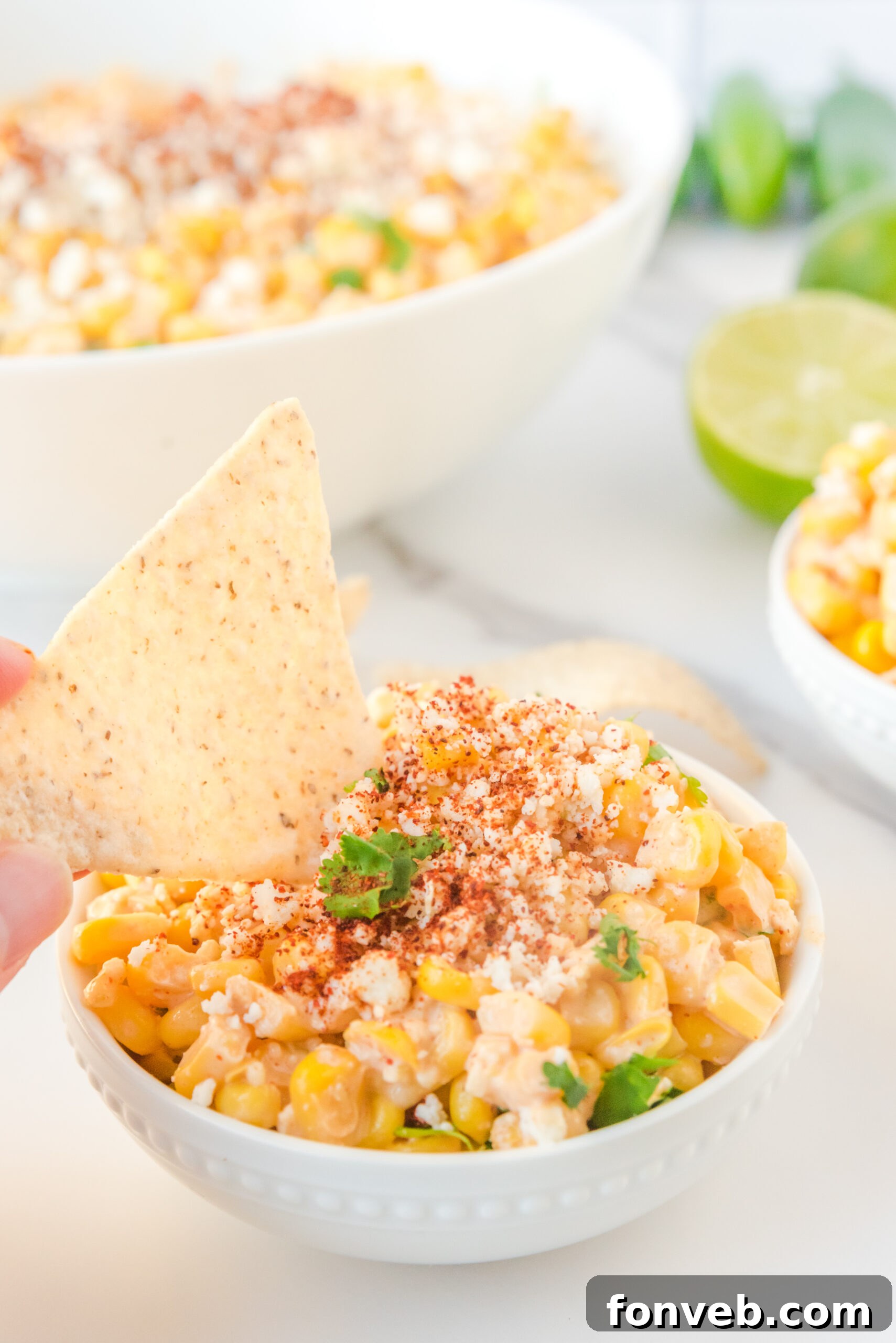 A crispy tortilla chip being dipped into a luscious serving of Mexican Street Corn Salad, highlighting its creamy texture.