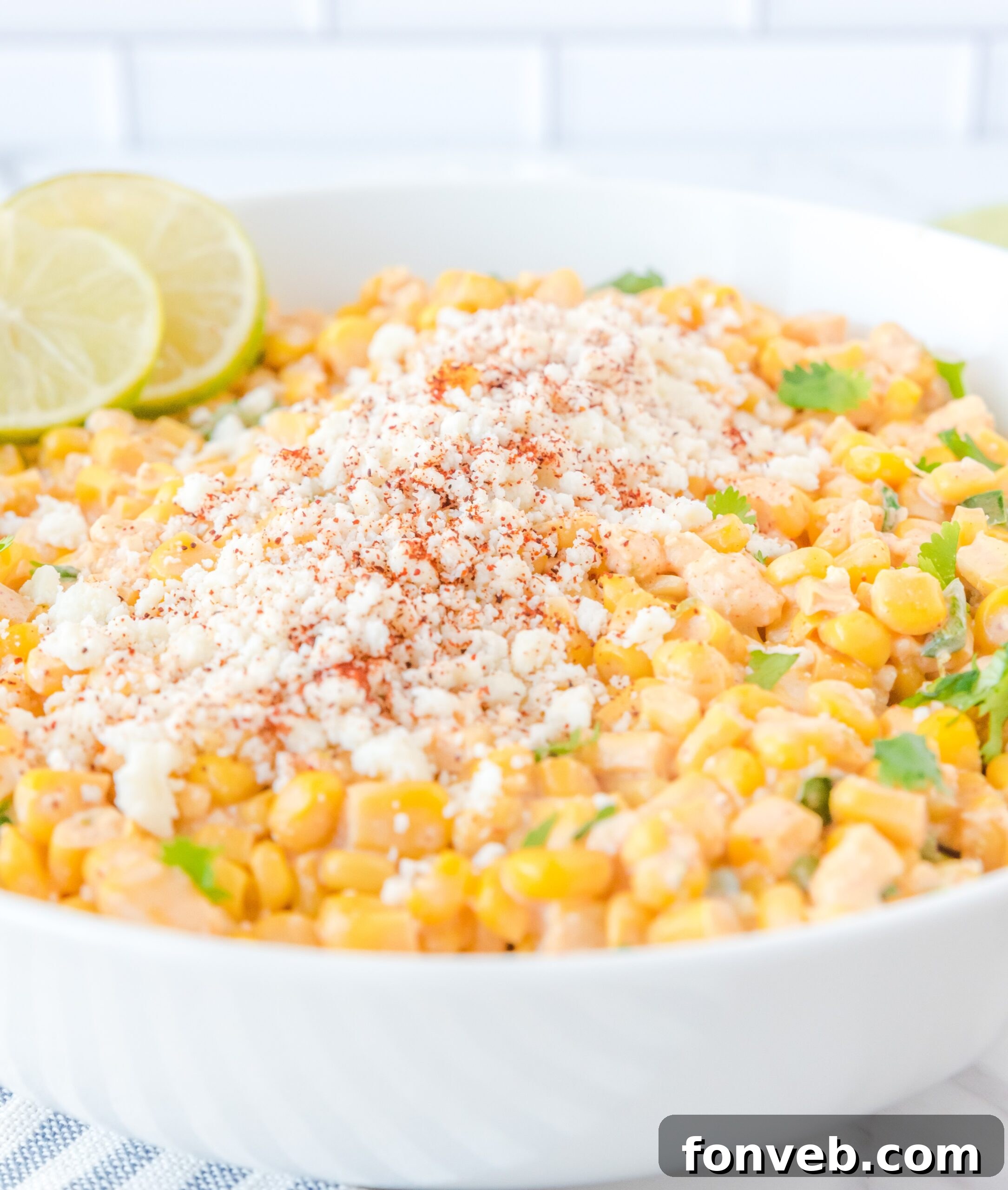 An inviting close-up of Mexican Street Corn Salad presented in a pristine white serving bowl, elegantly topped with crumbled feta cheese and delicate lime slices.
