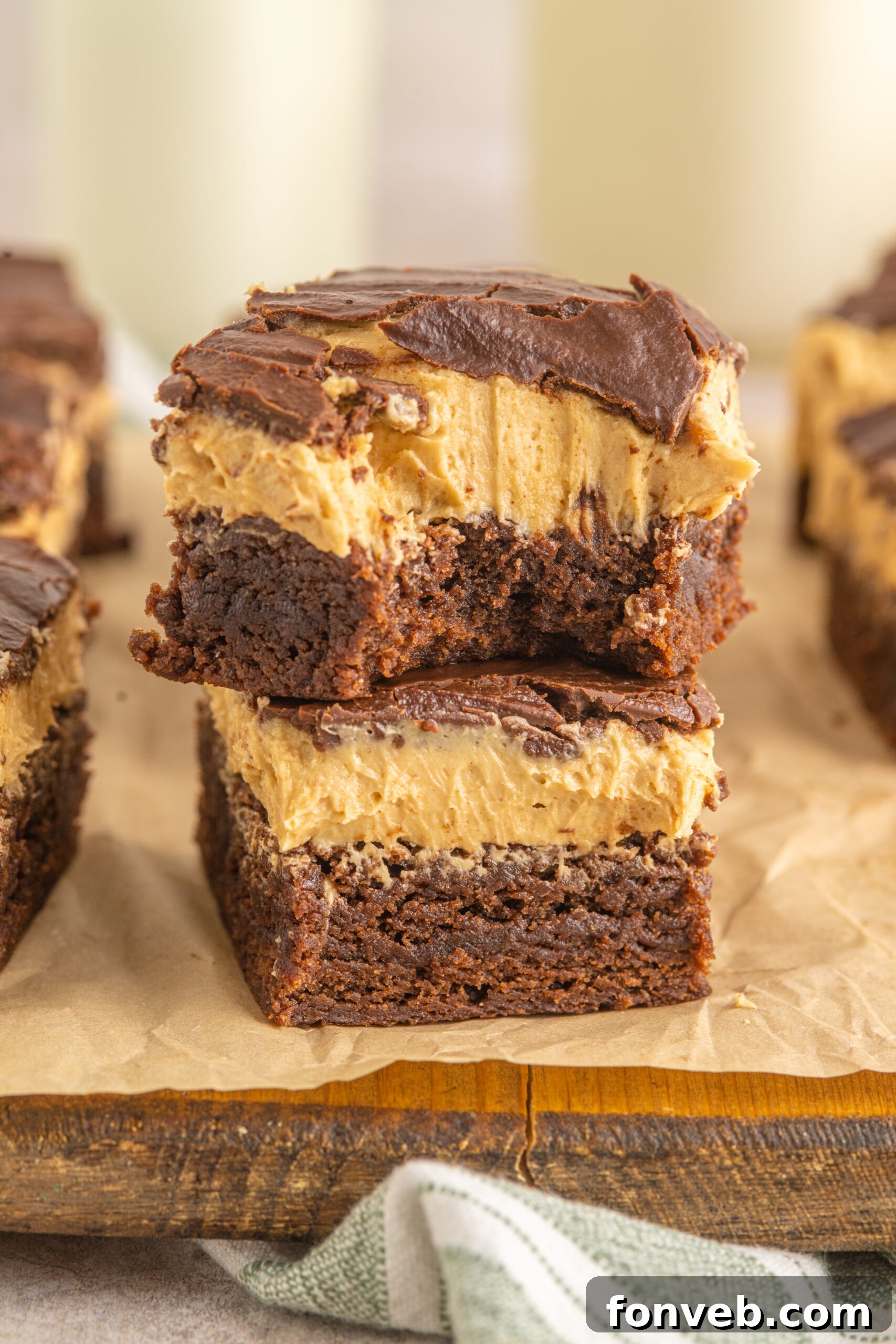 Two perfectly layered Buckeye Brownies, one with a bite taken out, showcasing the chocolate, peanut butter, and brownie layers.
