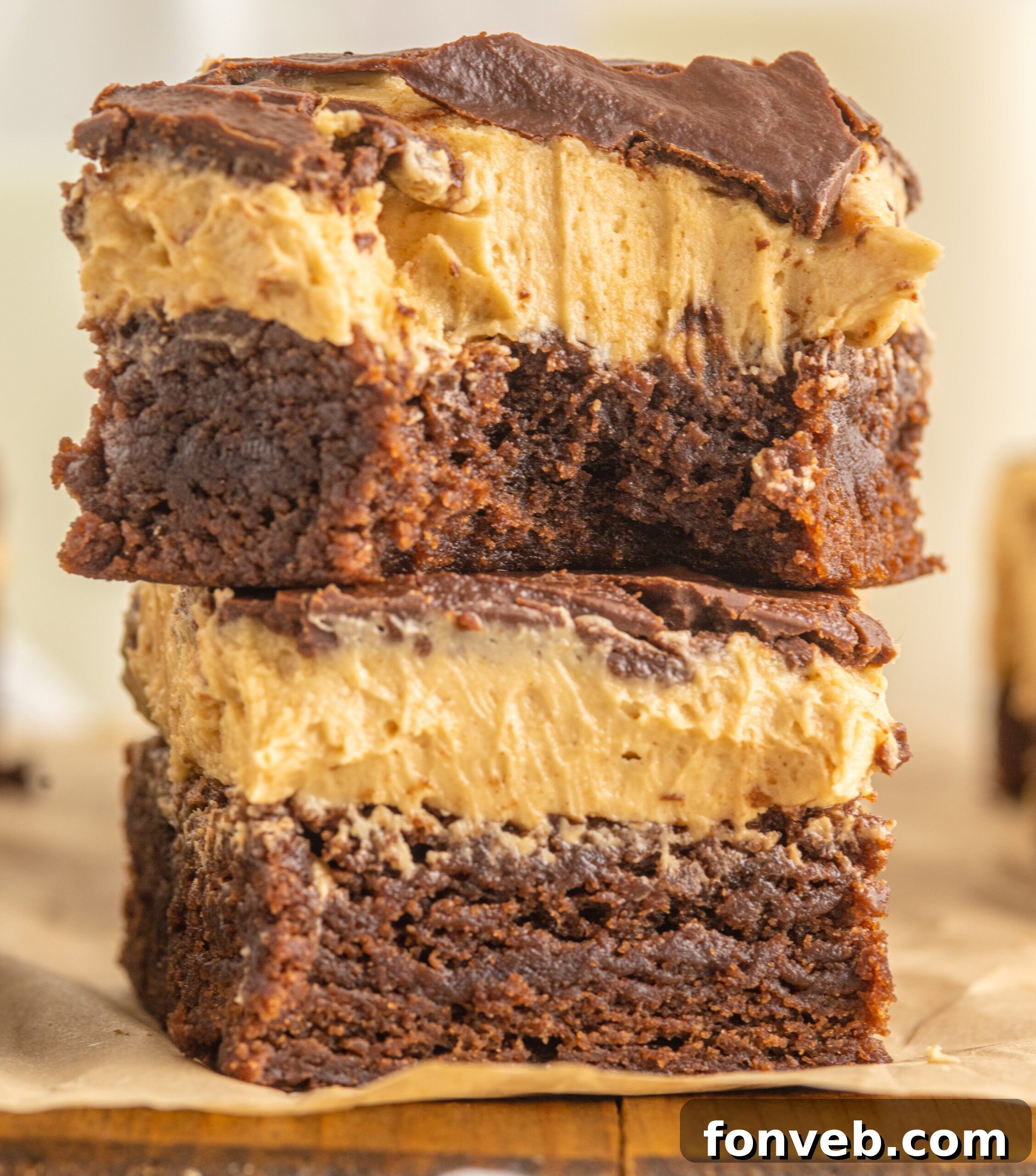 A close-up view of two stacked Buckeye Brownies, revealing the distinct layers of brownie, peanut butter, and glossy chocolate ganache.