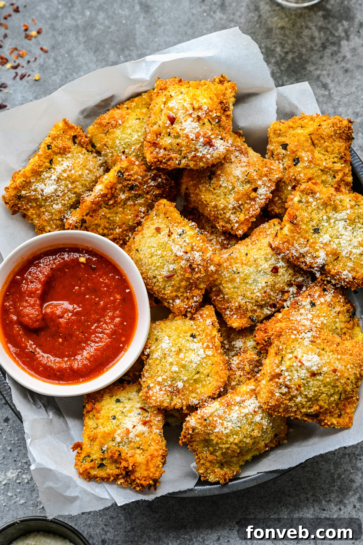Overhead view of Air Fryer Ravioli in a black serving tray with parchment paper and marinara sauce. 
