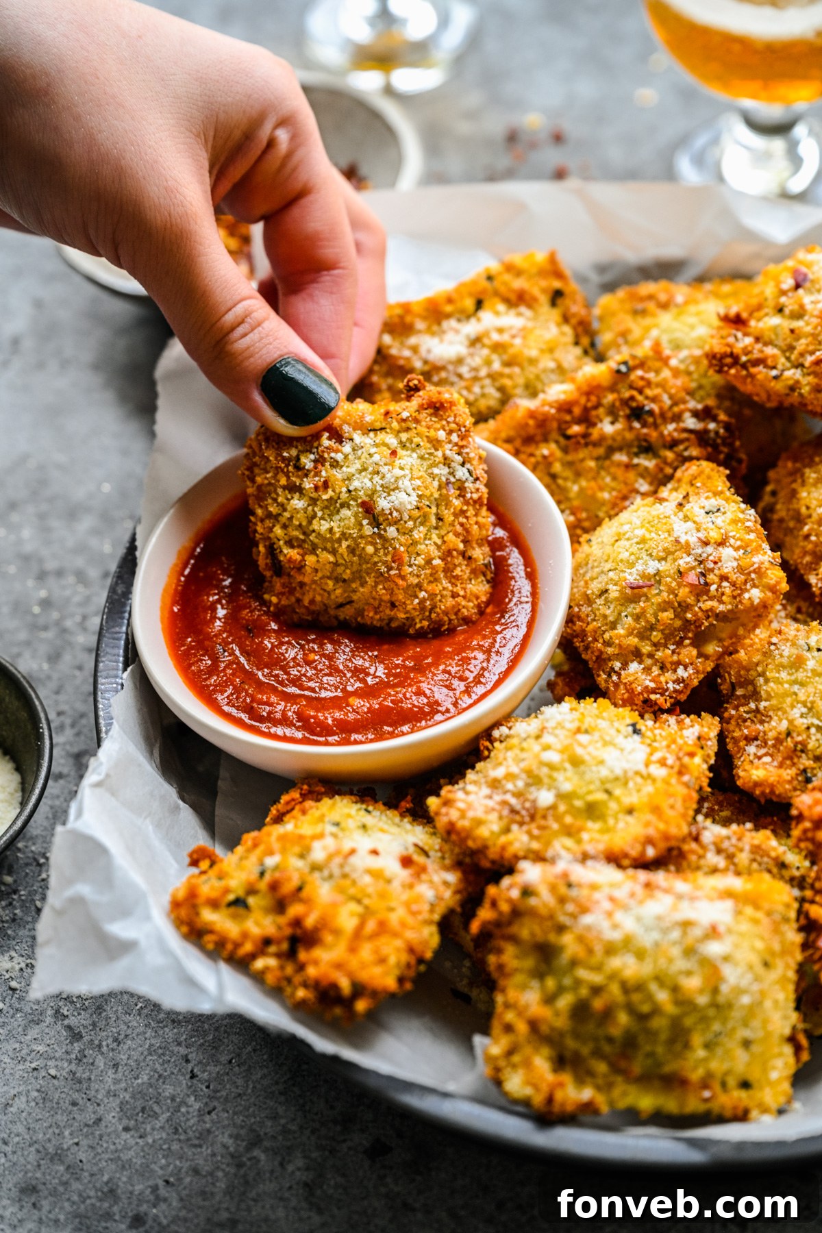 A hand dipping an air fryer ravioli into marinara sauce. 