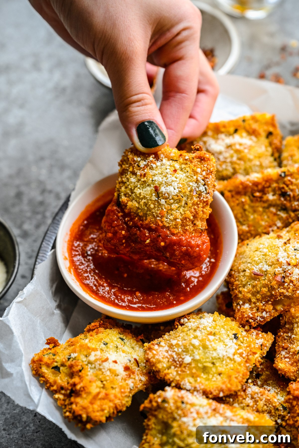 A hand dipping an air fryer ravioli into marinara sauce. 